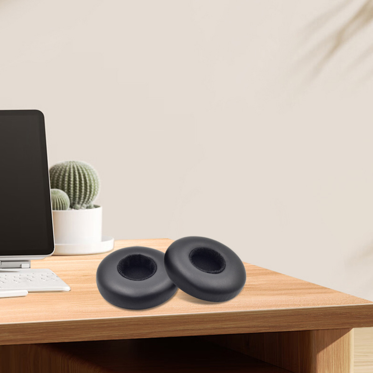 Twee zwarte koptelefoon oorkussens op een houten bureau met computer.