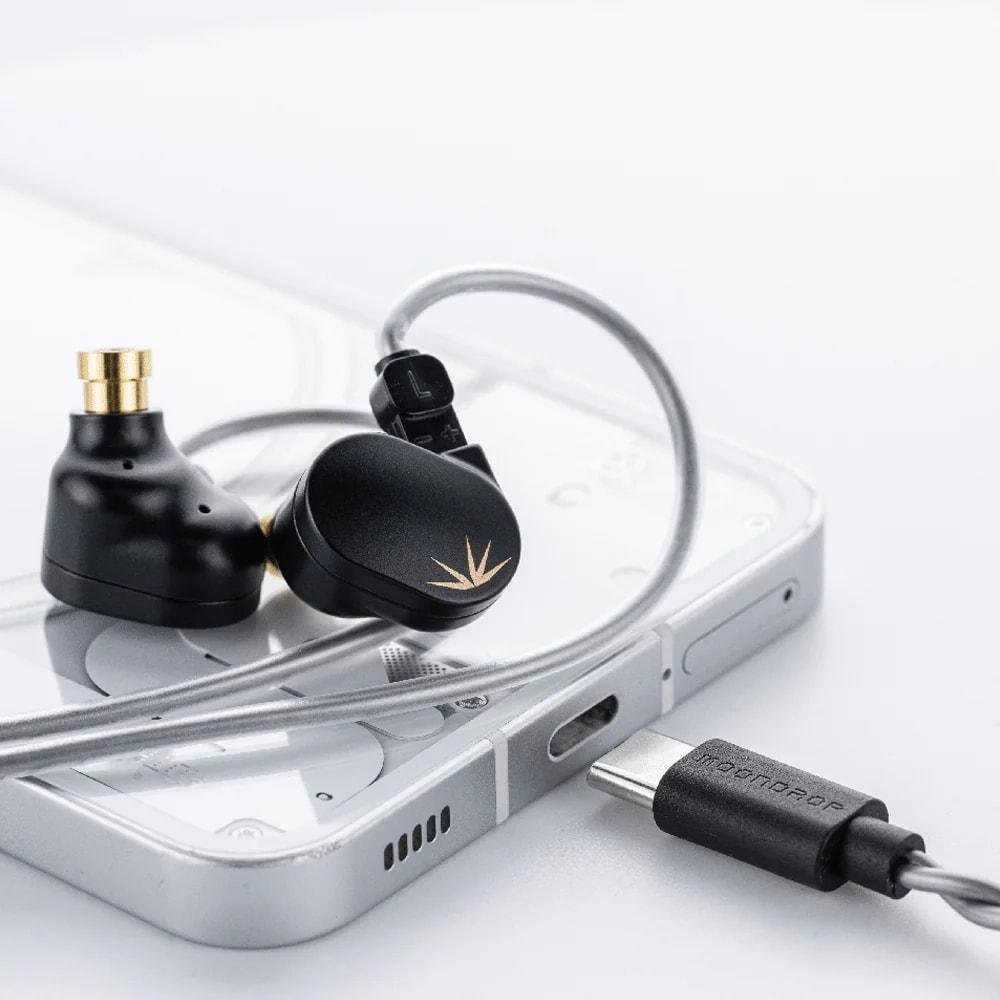Auricolari neri con accenti dorati su una custodia trasparente per telefono, collegati a un cavo USB-C.
