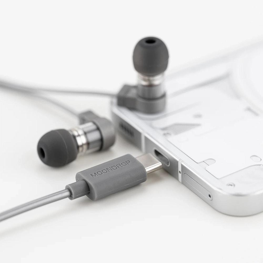 Gümüş renkli bir cihaza takılı USB-C konektörlü gri kulaklıklar.
