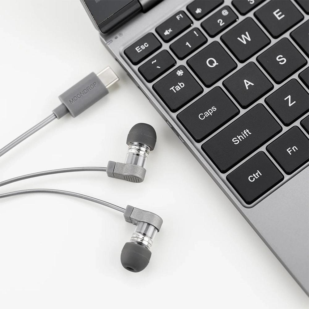 USB-C konnektörlü gri kulaklık, laptop klavyesinin yanında duruyor.