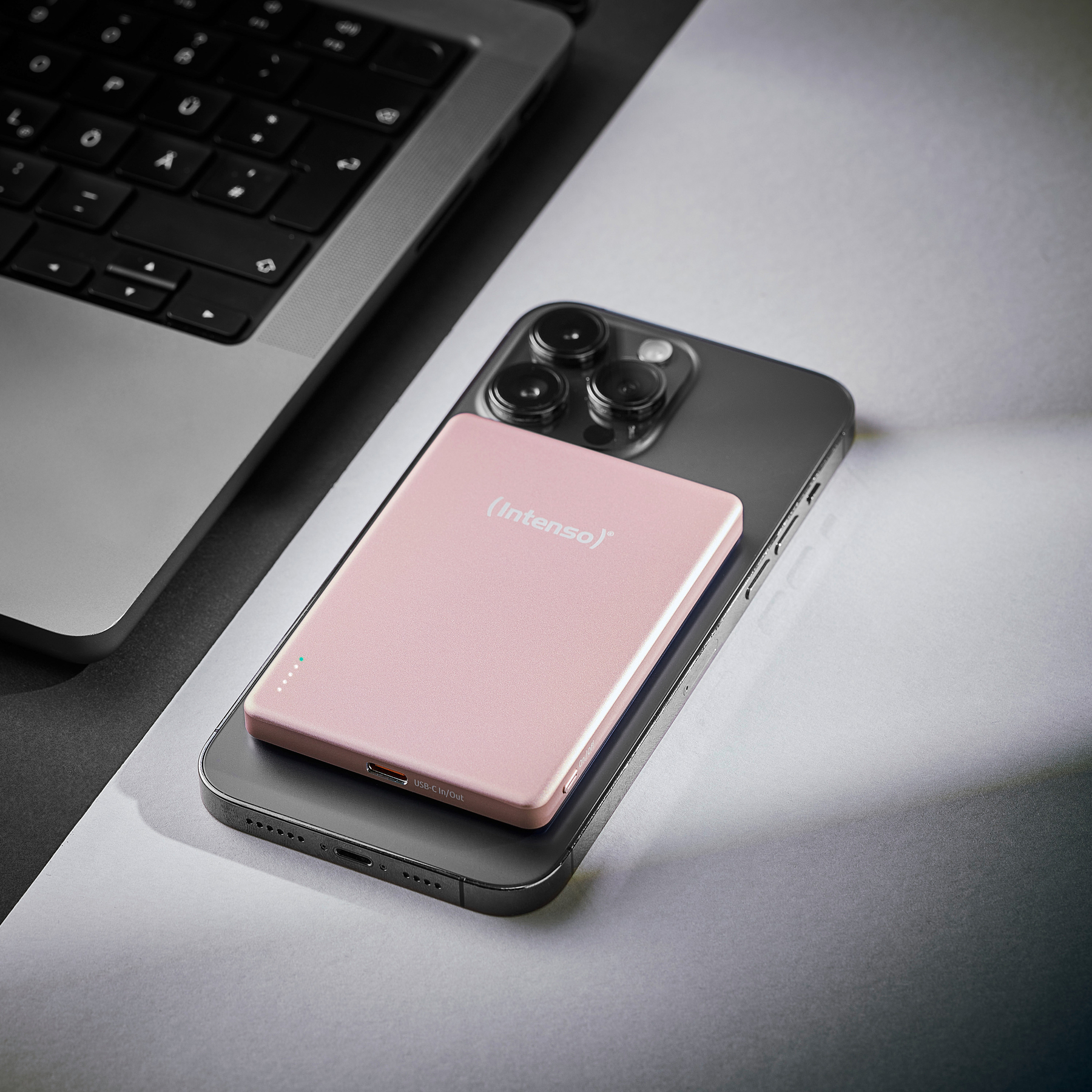 Ein rosa Ladegerät liegt auf einem dunklen Smartphone neben einem Laptop.