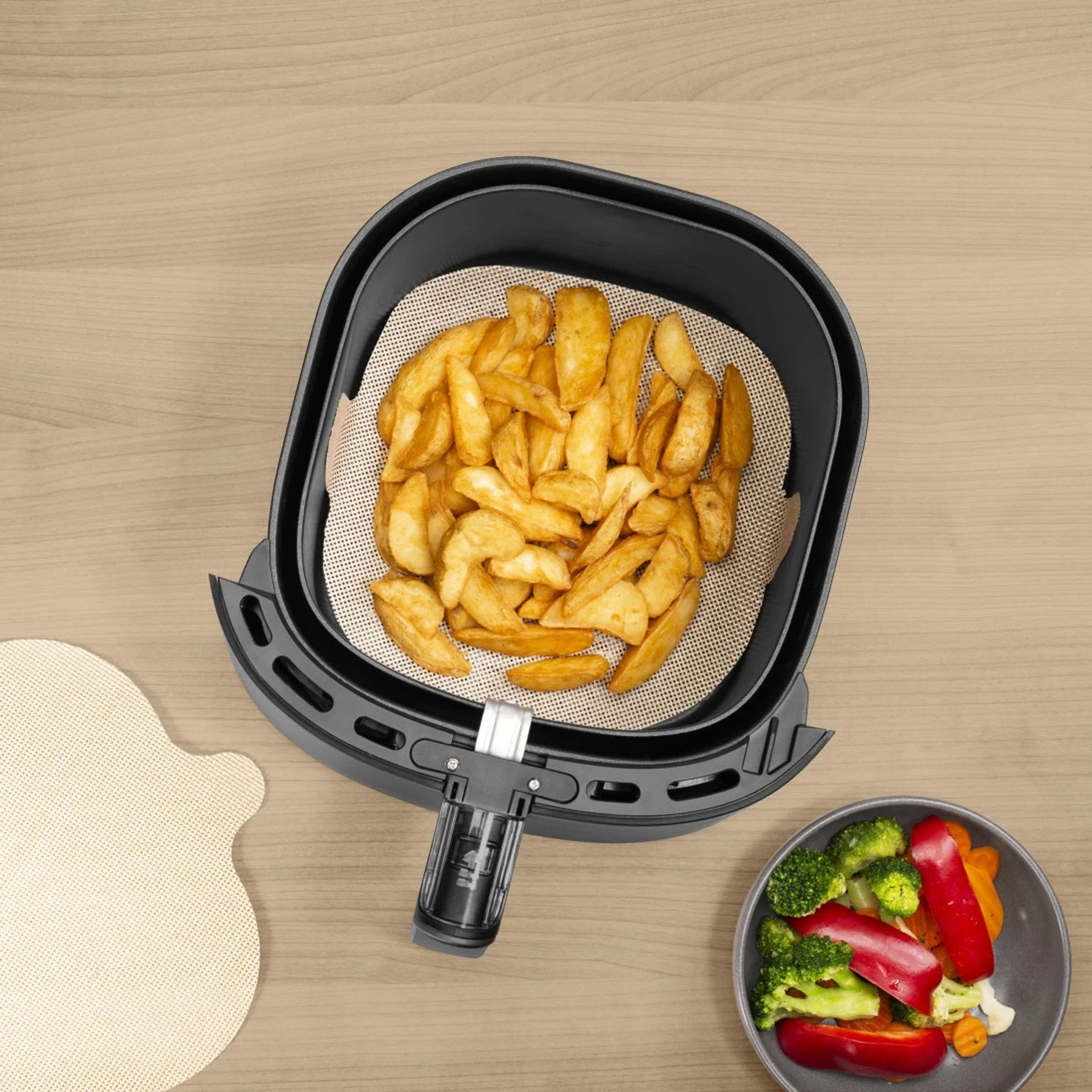 Ein Airfryer mit Pommes und ein Schälchen mit Gemüse auf einem Holztisch.