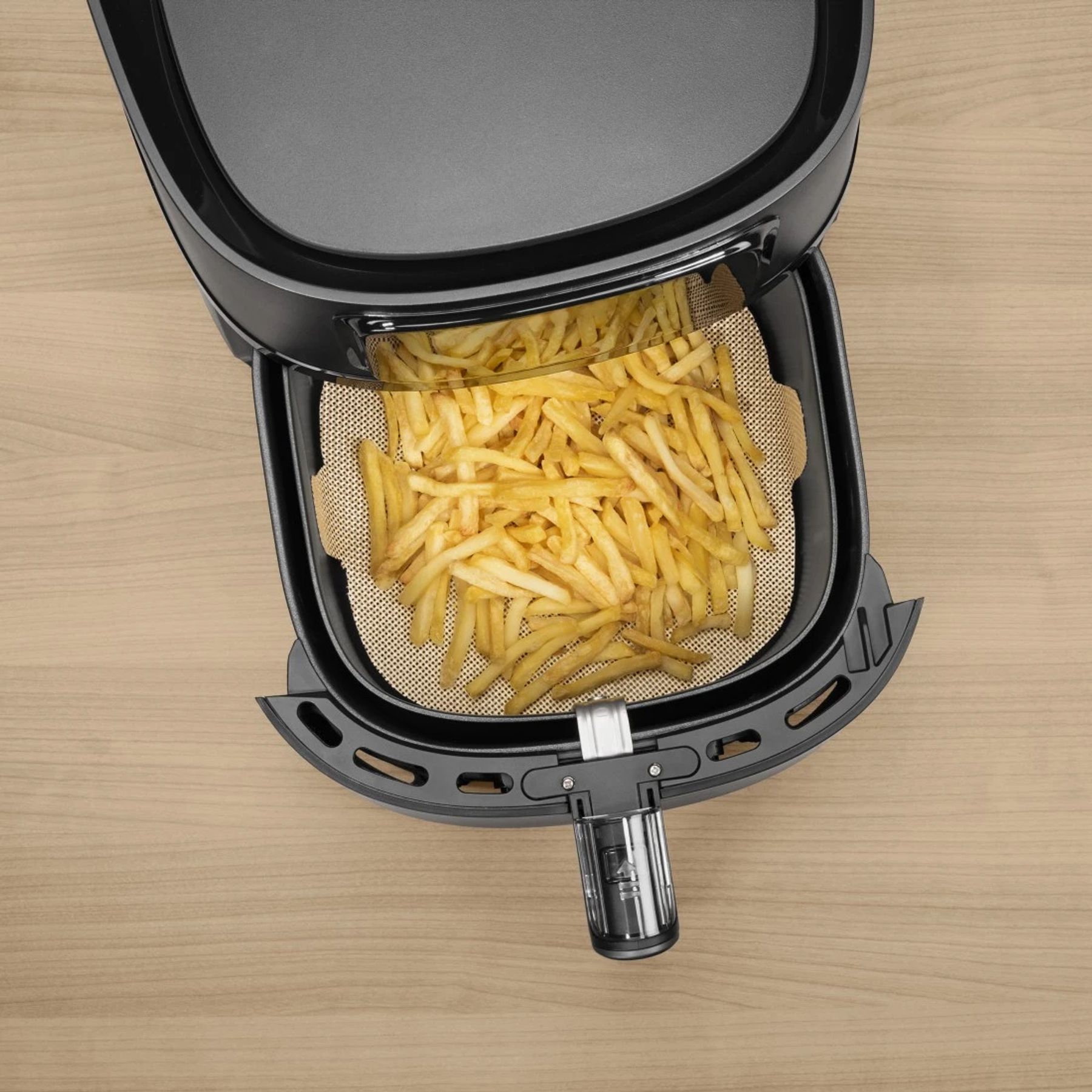 Frittierte Pommes in einem schwarzen Heißluftfritteusenkorb auf Holztisch.