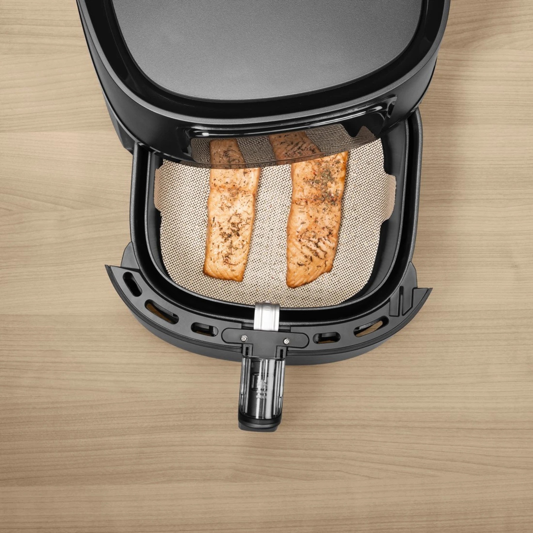 Zwei Lachsfilets in einem Airfryer auf einem perforierten Einsatz, gewürzt.