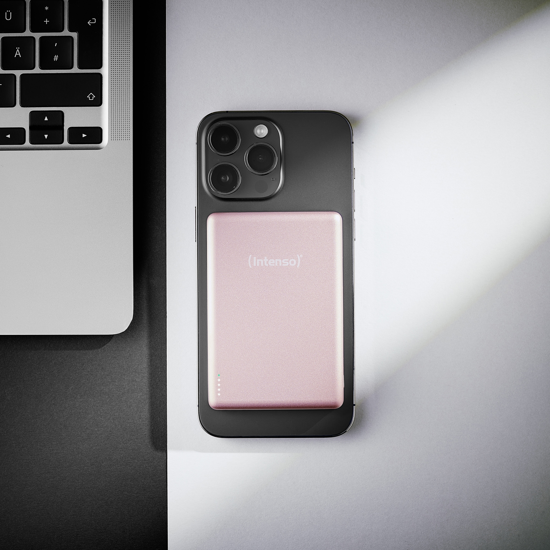 Ein schwarzes iPhone mit einer rosafarbenen Powerbank daneben, neben einem Laptop.