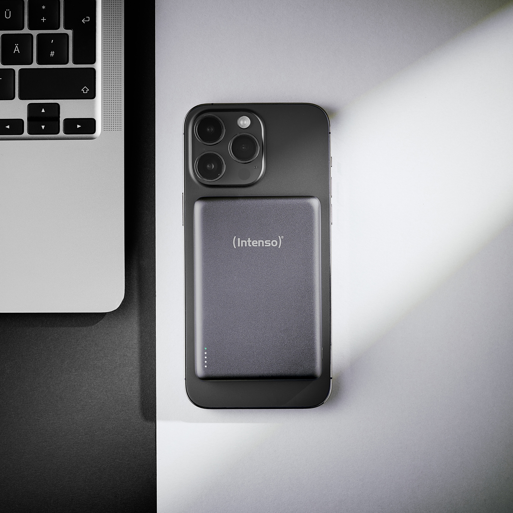 Ein Smartphone mit Powerbank und Laptop daneben auf einem Tisch.