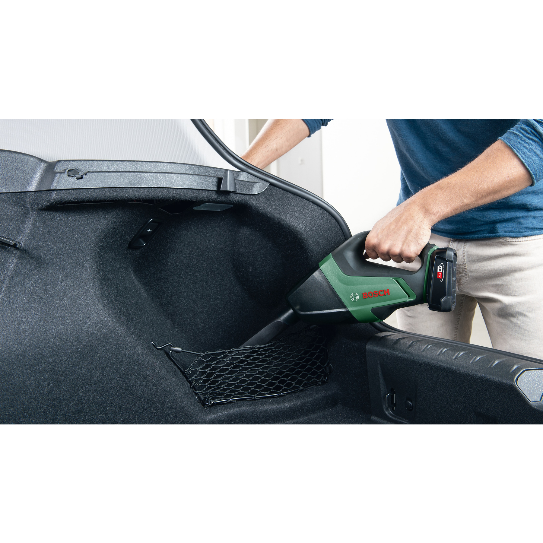 Un hombre aspira el maletero de un coche con una aspiradora Bosch verde.