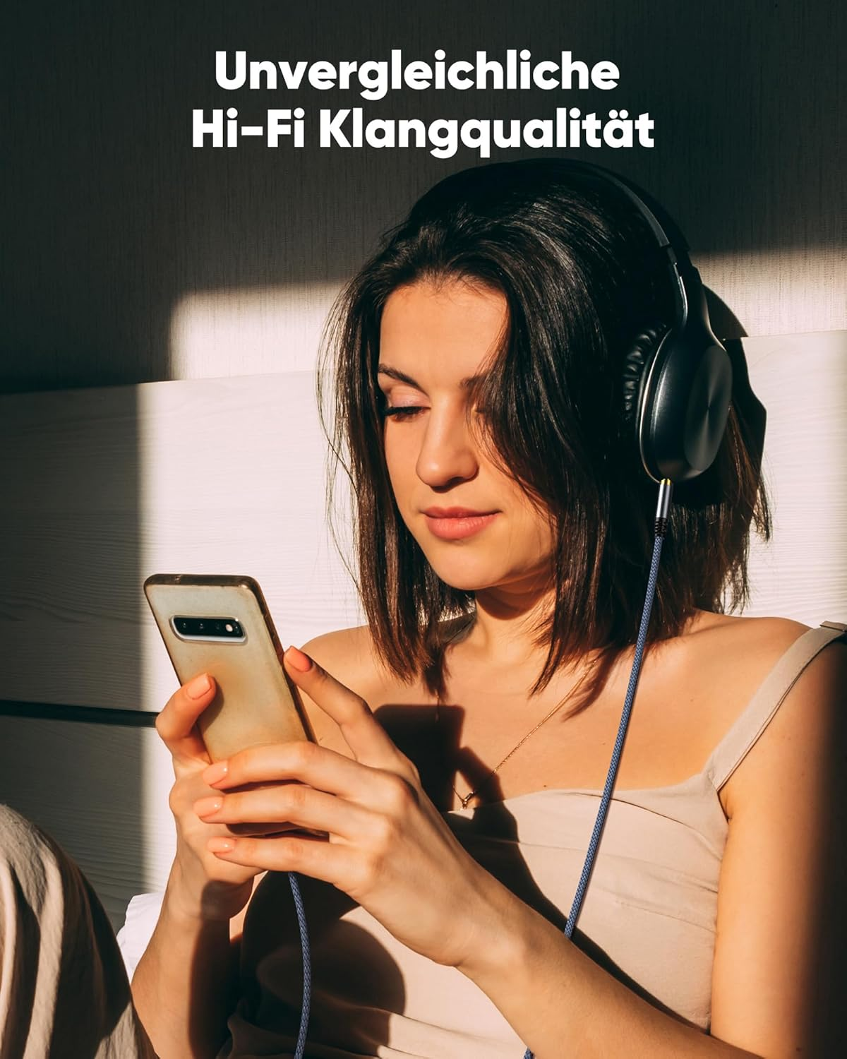 Giovane donna con cuffie e telefono in una stanza soleggiata.