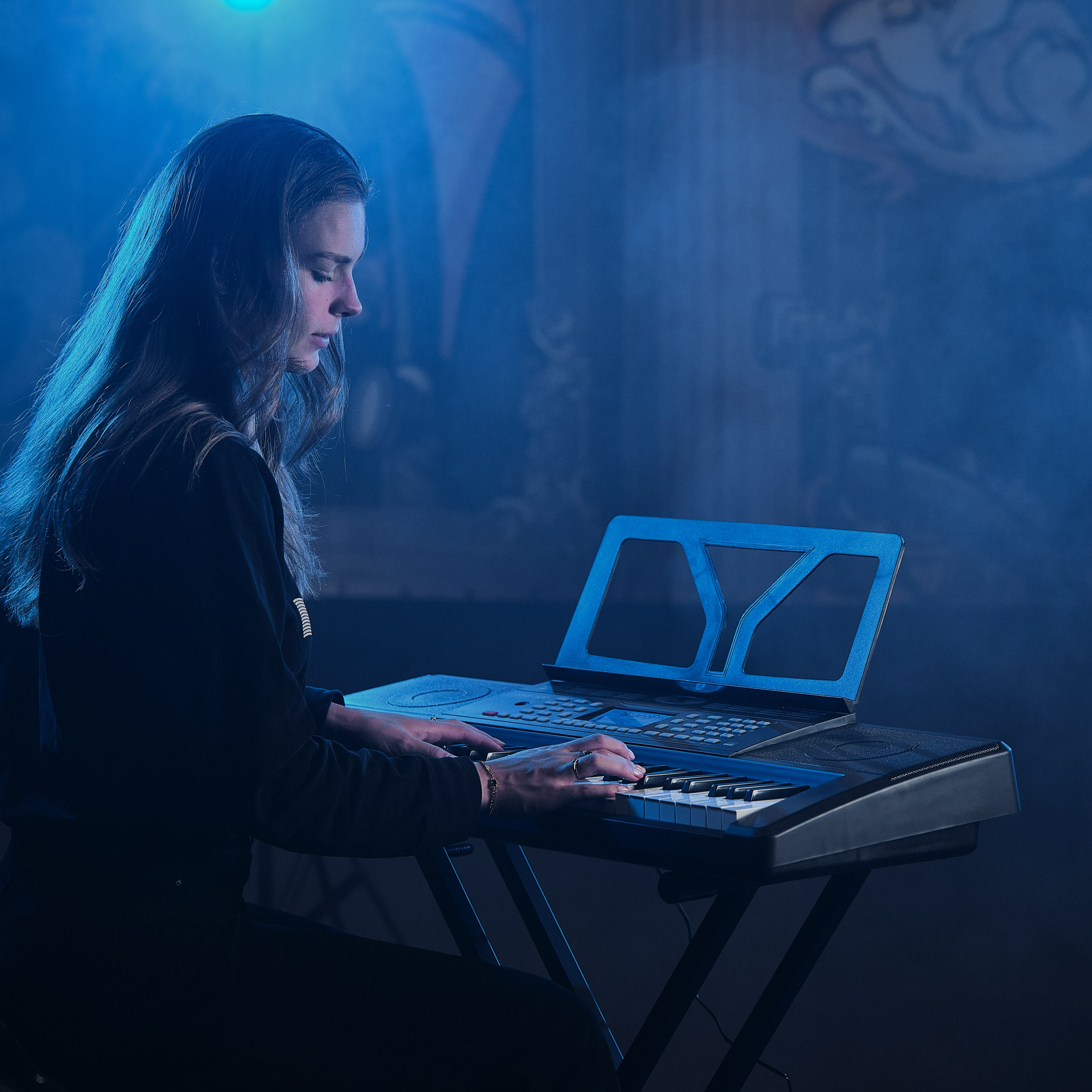 Een vrouw speelt keyboard in blauw licht, met mist op de achtergrond.