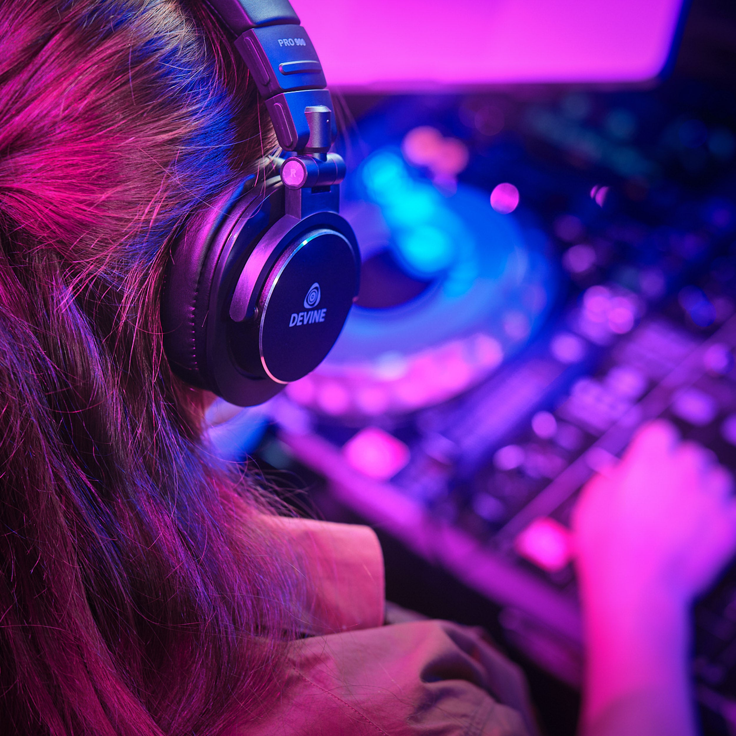DJ met koptelefoon en mixer, verlicht door paarse en blauwe lichten.