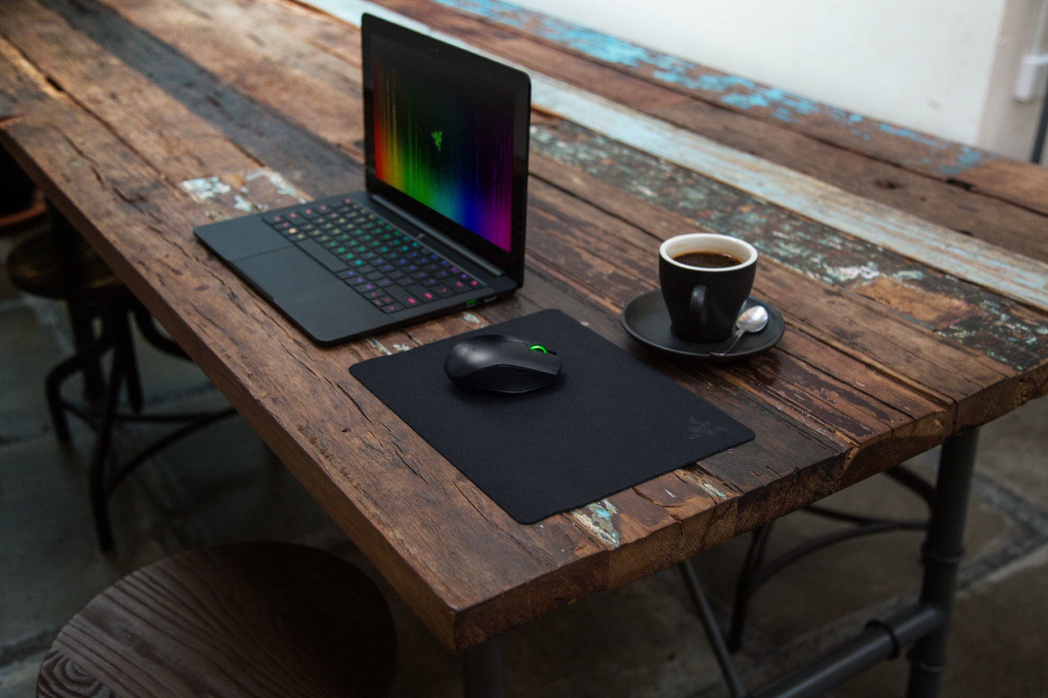 Un laptop con illuminazione arcobaleno, un mouse su un tappetino e una tazza di caffè.