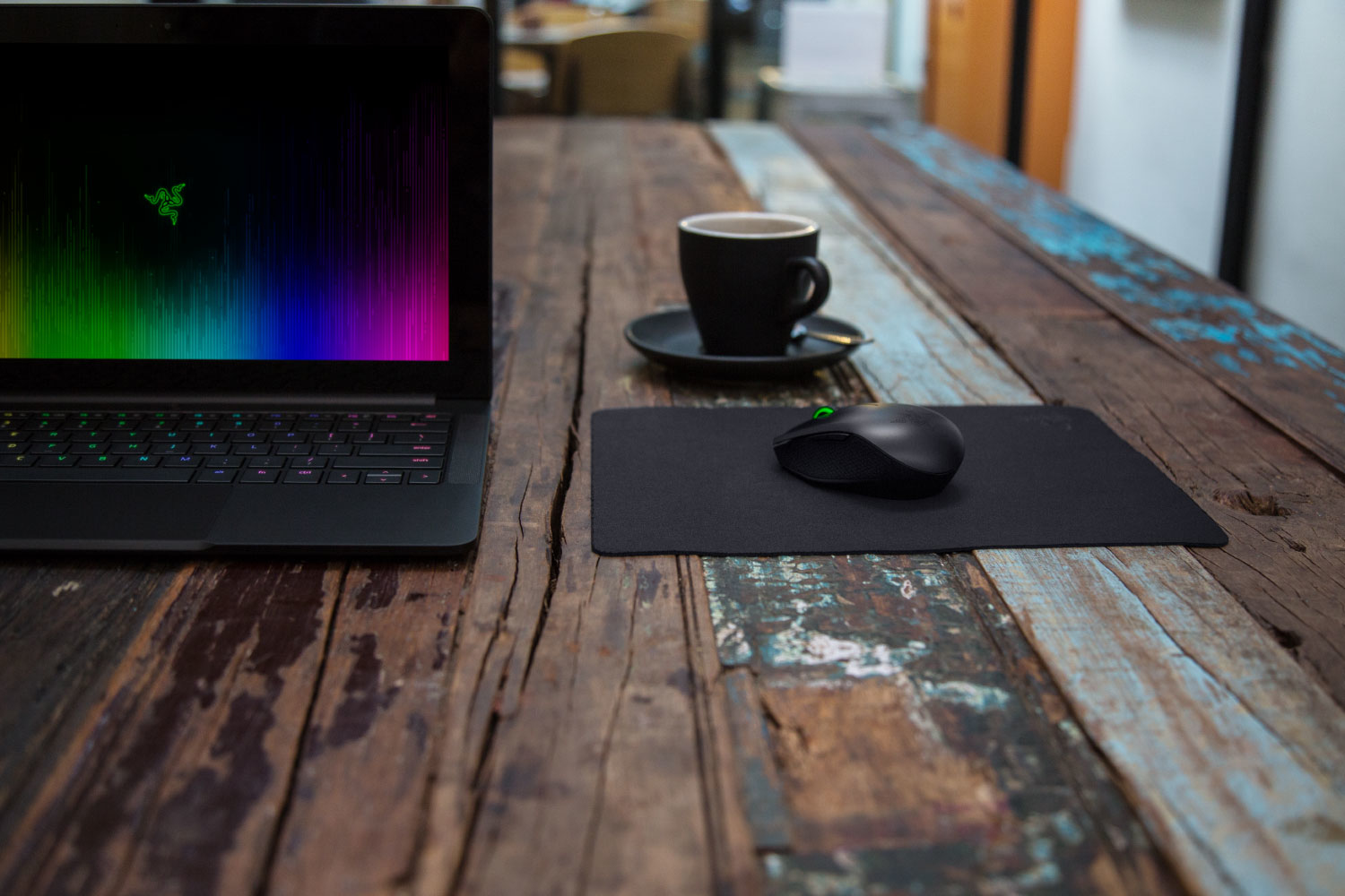 Un laptop nero con schermo arcobaleno è su un tavolo di legno accanto a una tazza di caffè e un mouse.