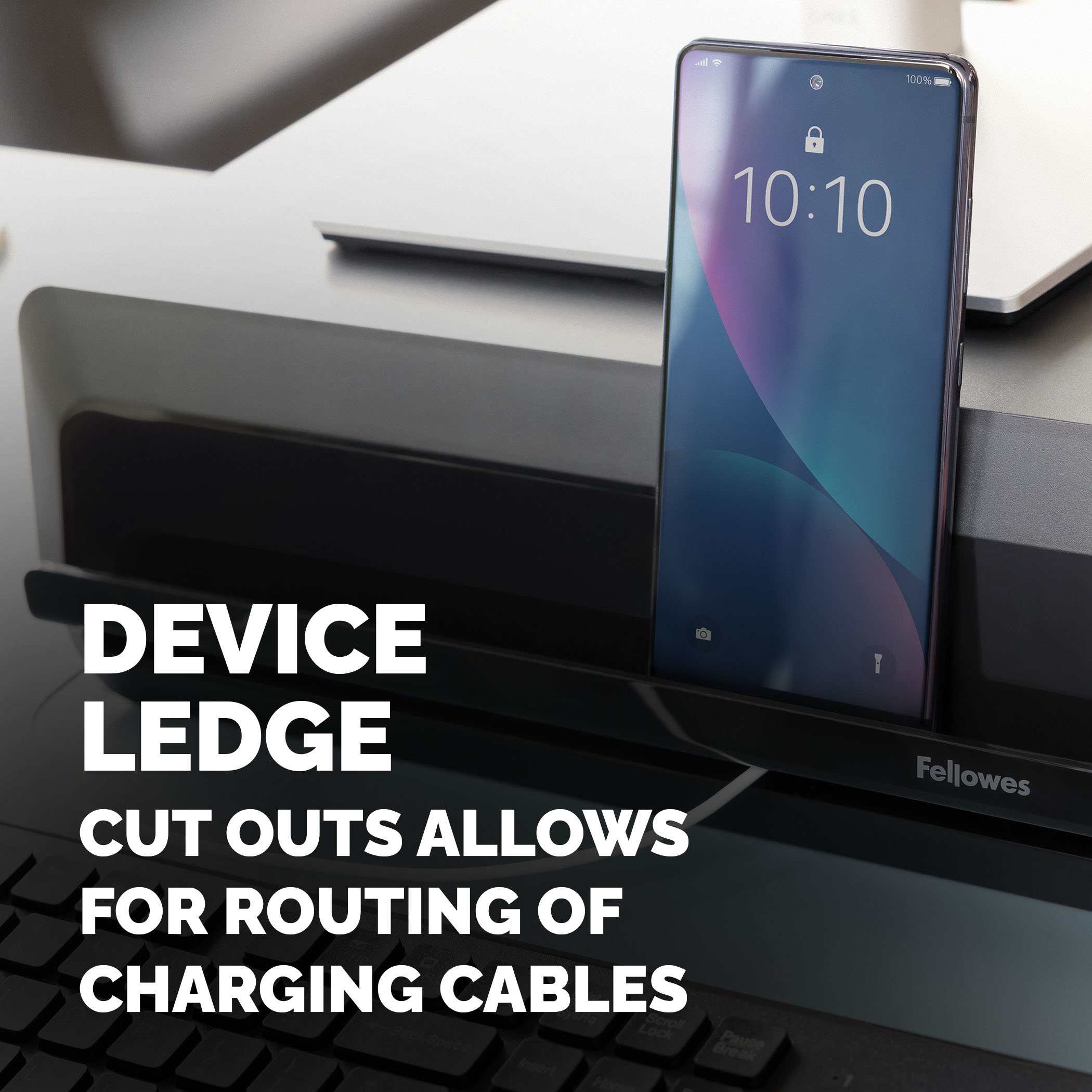 Smartfon stoi na czarnej półce Fellowes. Klawiatura pod spodem.