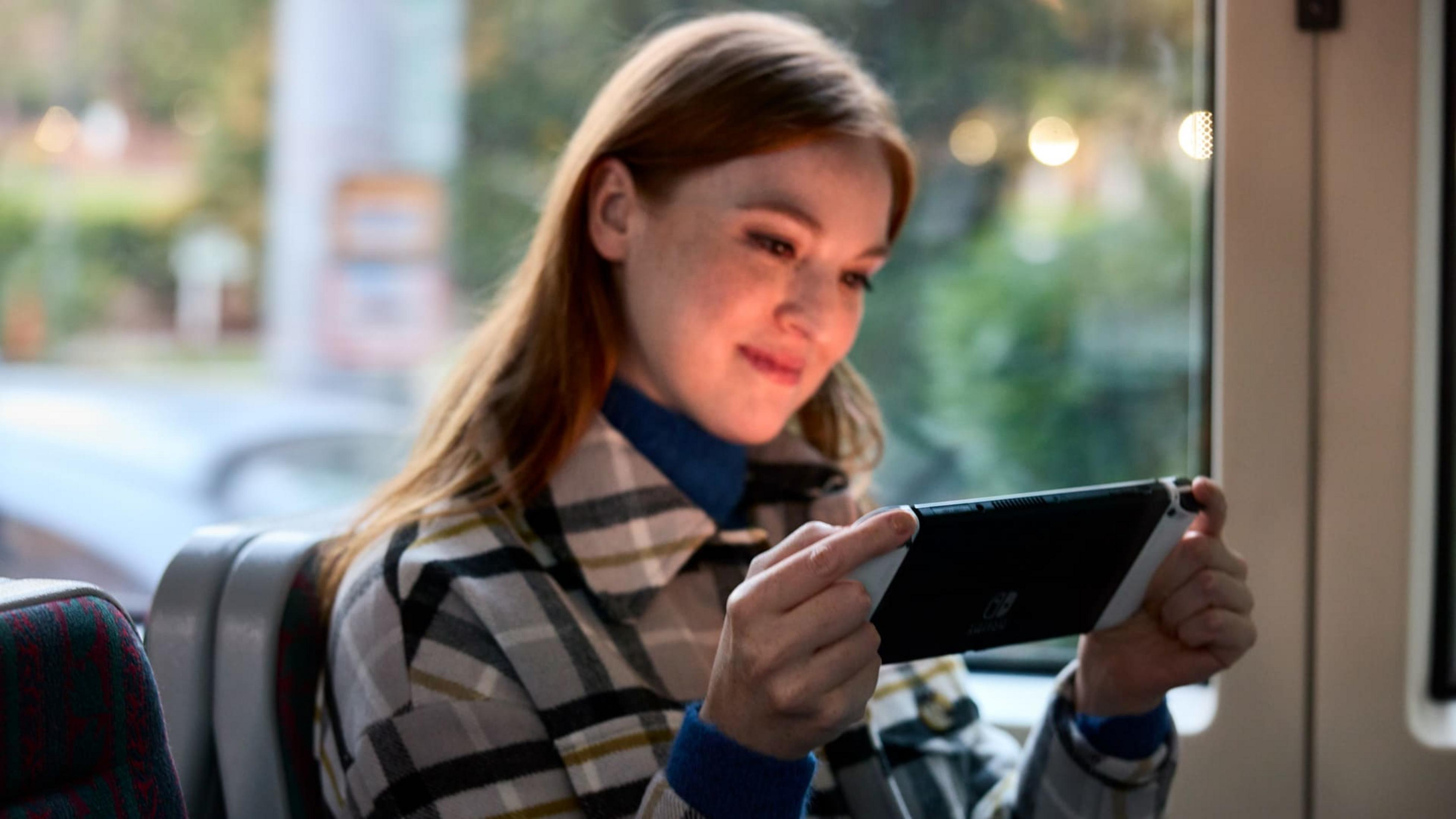 Kobieta z rudymi włosami gra na Nintendo Switch w autobusie.