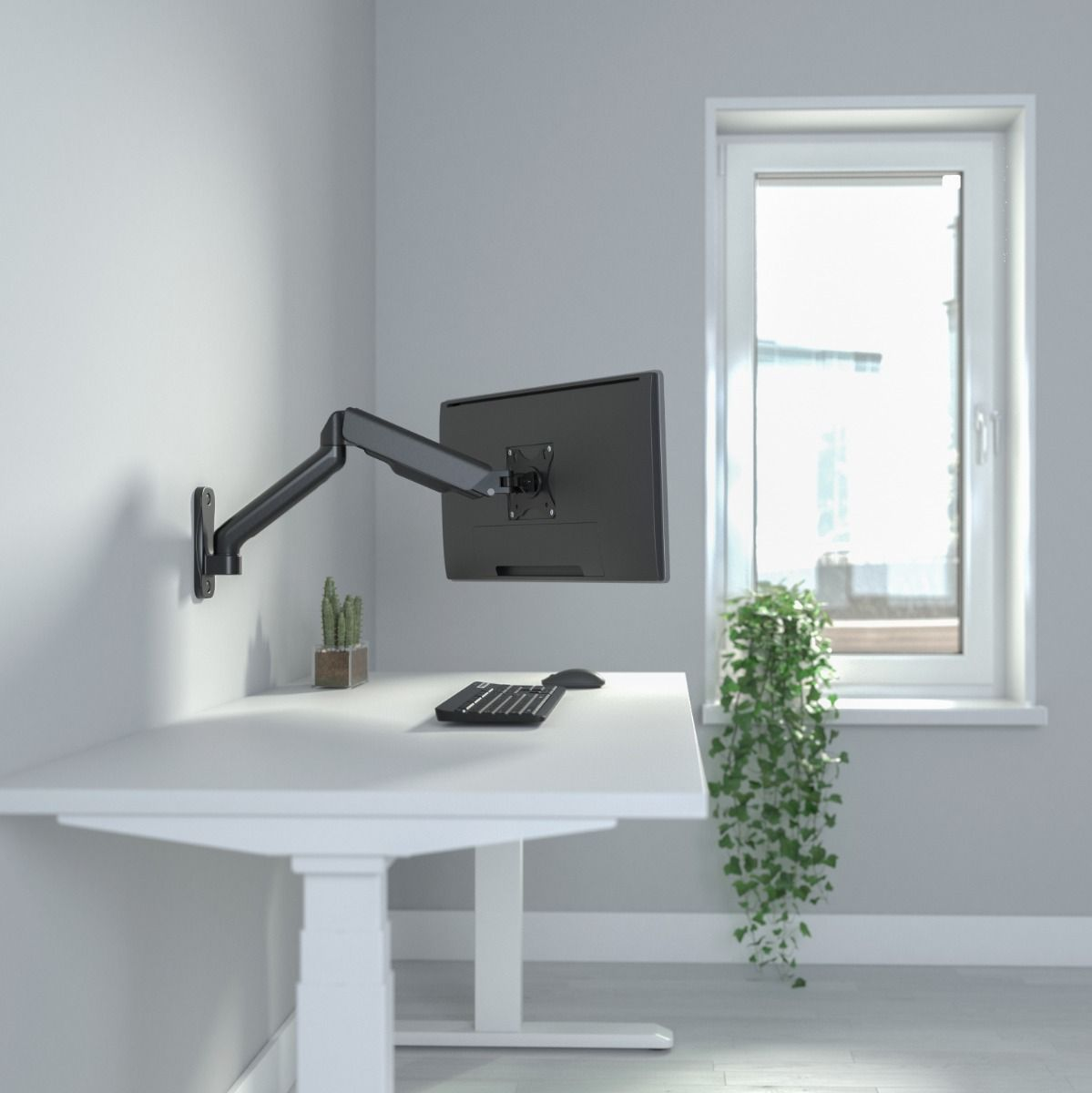 Ein Monitor ist an einem schwarzen Arm an der Wand befestigt, über einem Schreibtisch mit Tastatur und Maus.