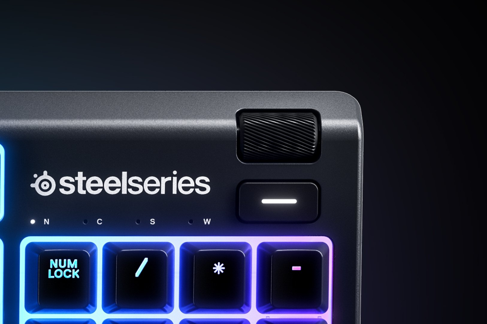 Primo piano di una tastiera Steelseries nera con tasti illuminati e una manopola rotante.