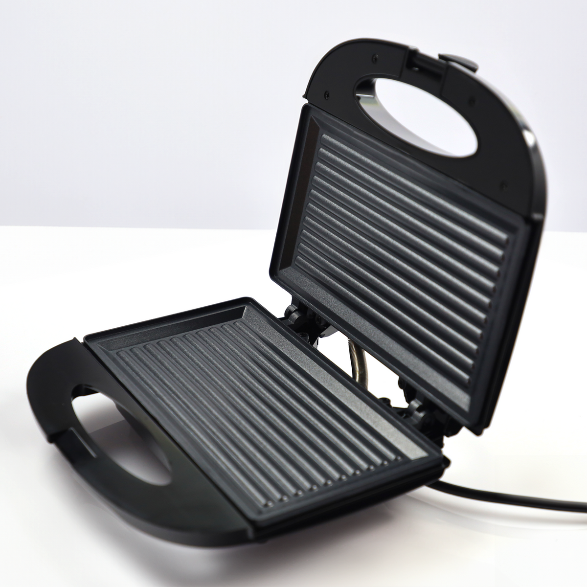 Otwarty czarny opiekacz do kanapek z ryflowanymi płytami grzewczymi na białym tle.