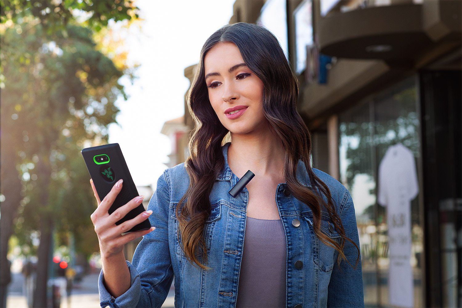 A woman with long hair holds a phone with a Razer logo and wears a microphone.