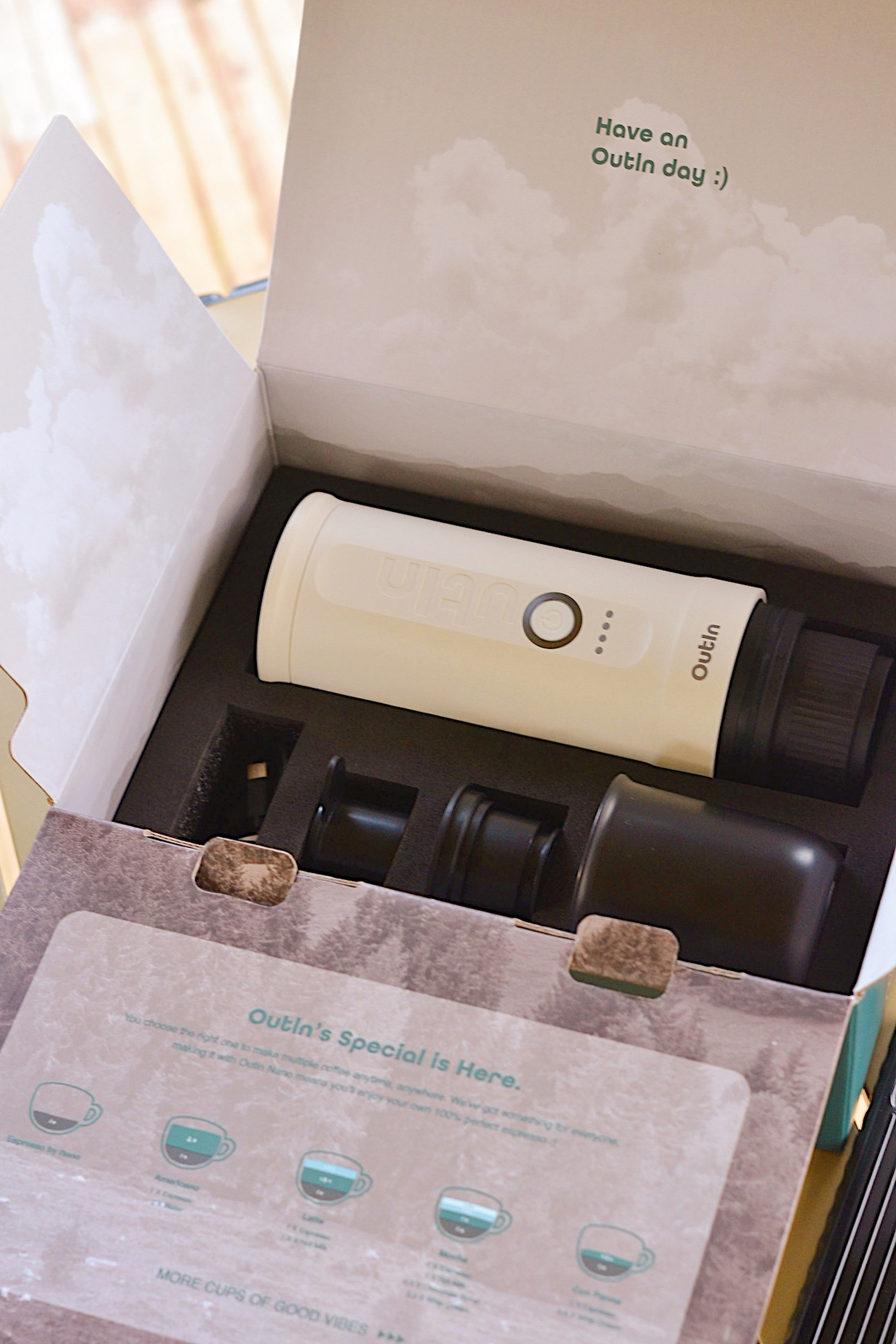 Een beige koffiezetapparaat met zwarte accessoires in een open doos.