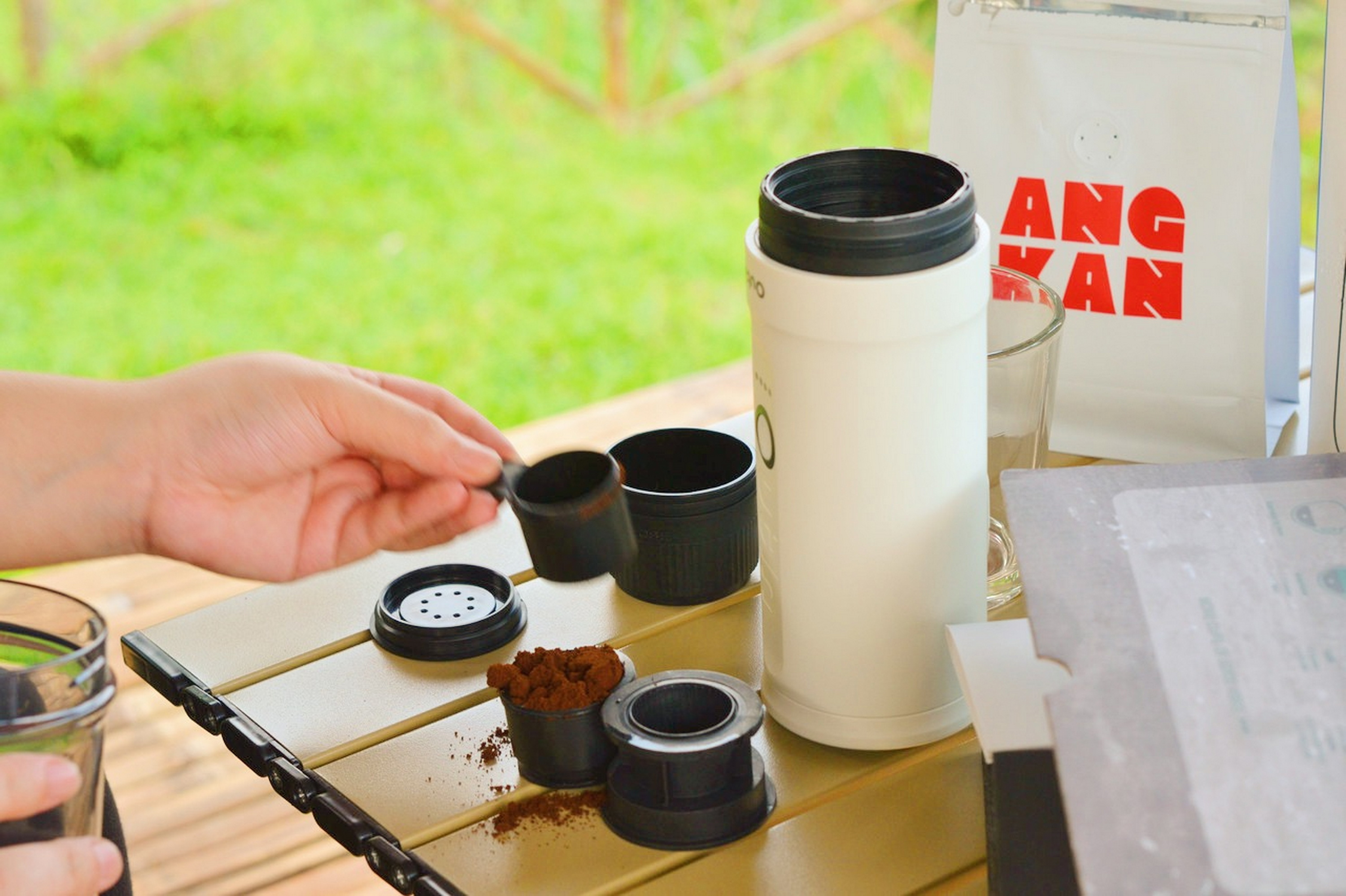 Een hand houdt een schep koffiepoeder boven een koffiezetapparaat.
