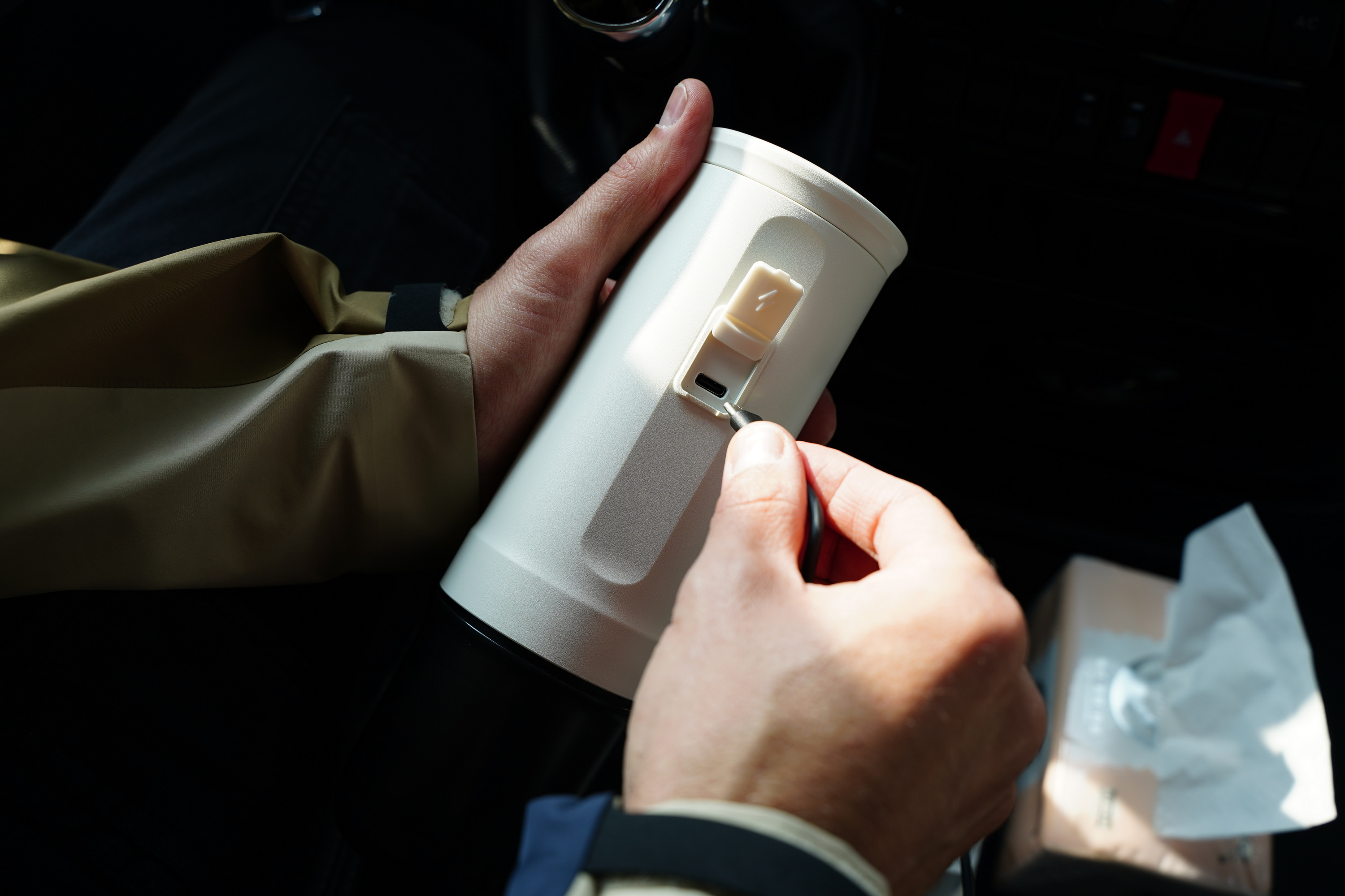Een hand steekt een kabel in een wit apparaat in een auto.