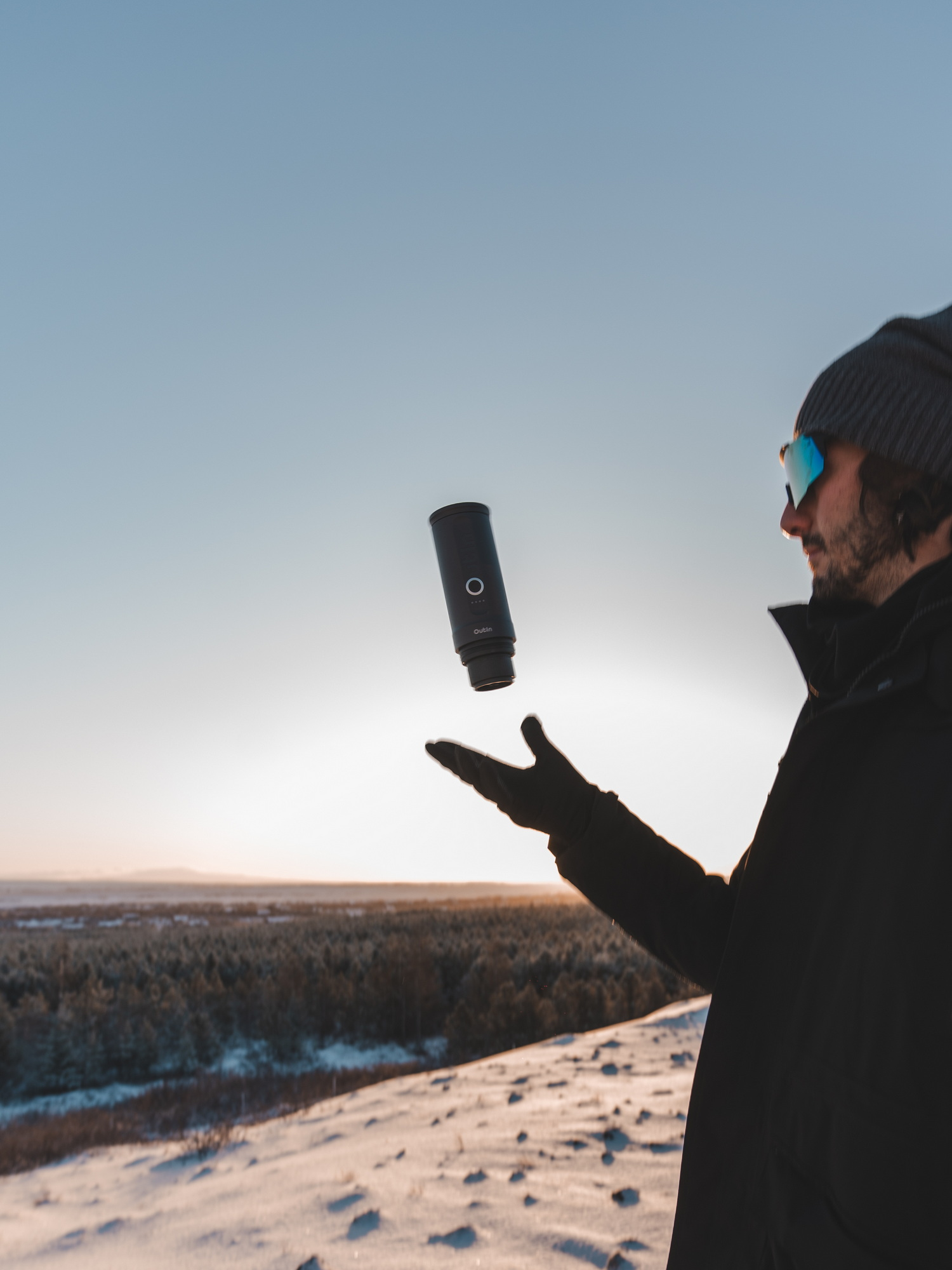 Man gooit een zwarte camera in de lucht in de sneeuw bij zonsondergang.