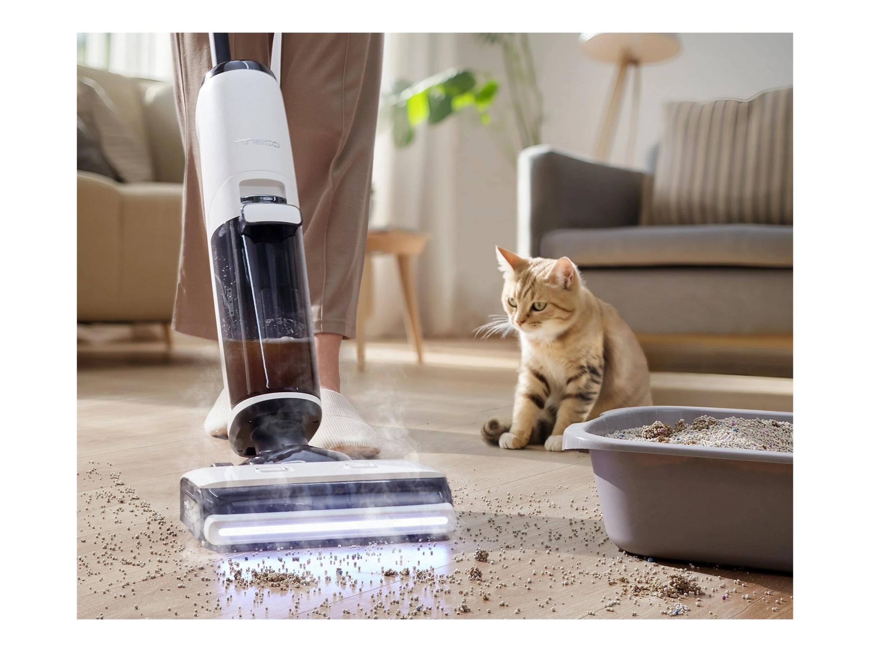 Ein Staubsauger reinigt einen holzboden, während eine Katze daneben sitzt.