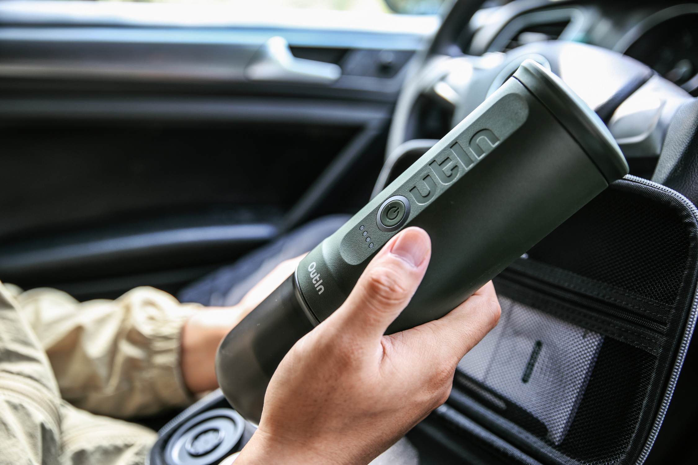 Een hand houdt een donkergroen apparaat met knoppen vast in een auto.