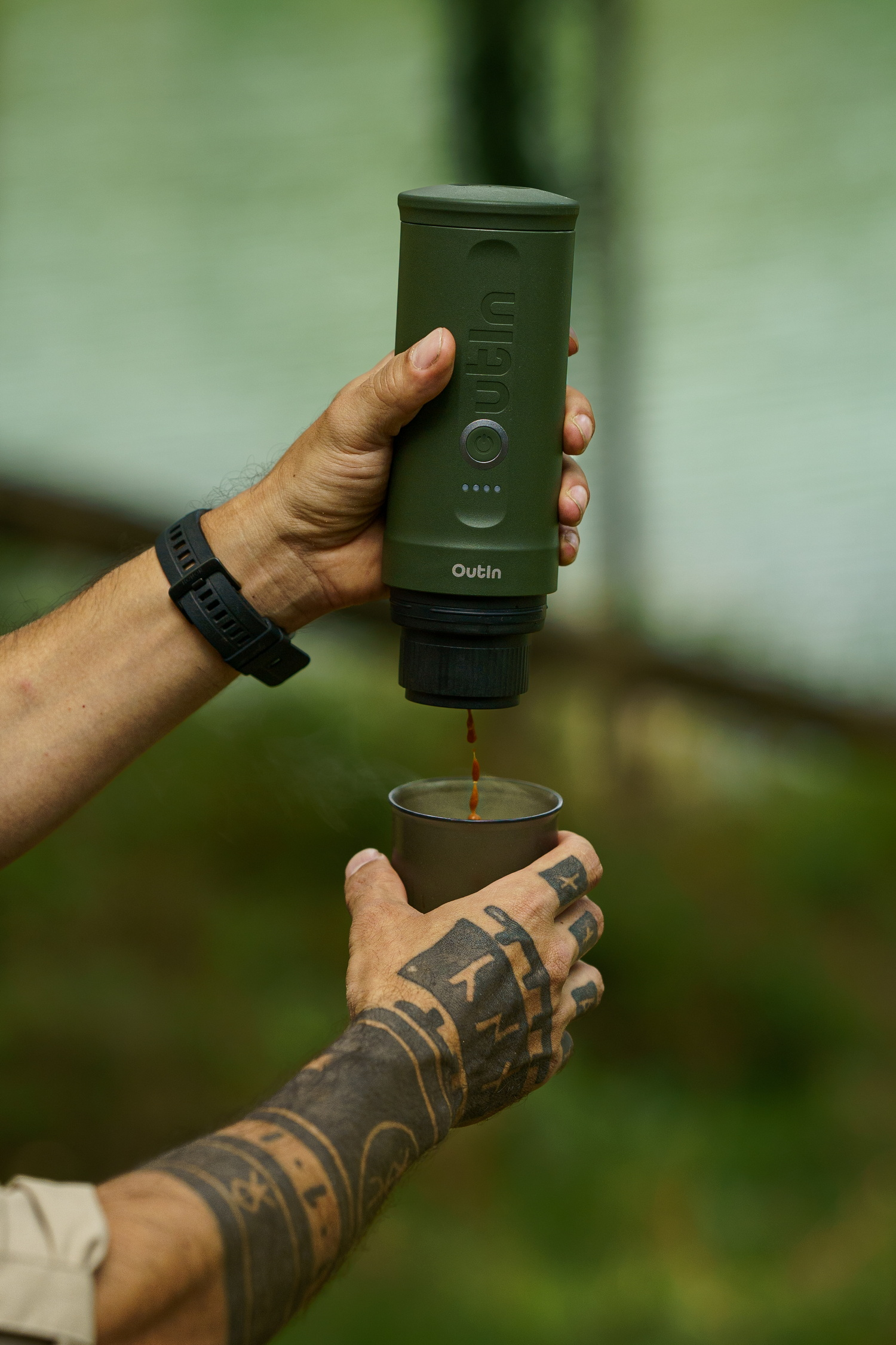 Een persoon schenkt koffie uit een groen Outin-apparaat in een kopje.
