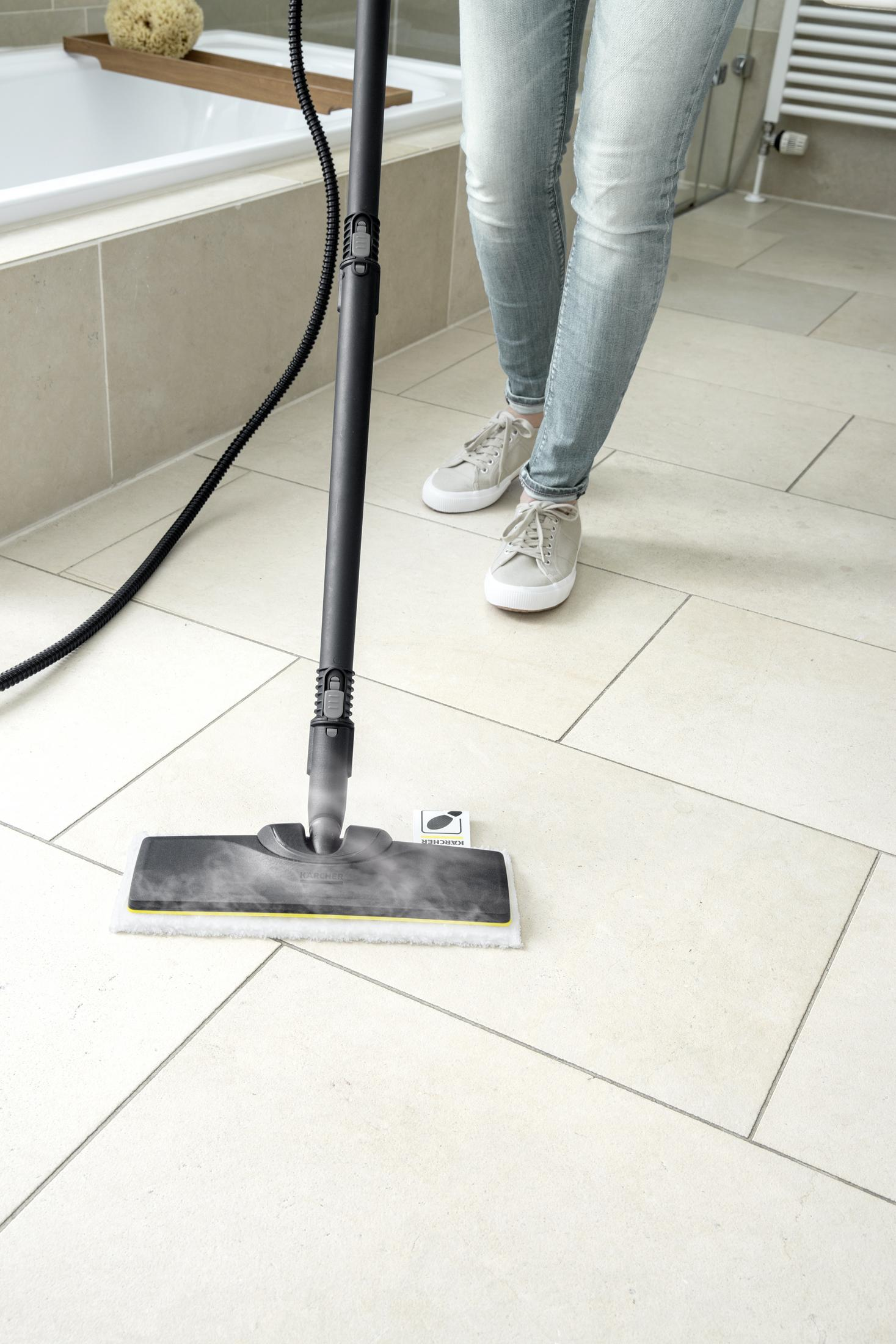 Bir kişi buharlı temizleyici ile fayanslı banyo zeminlerini temizliyor.