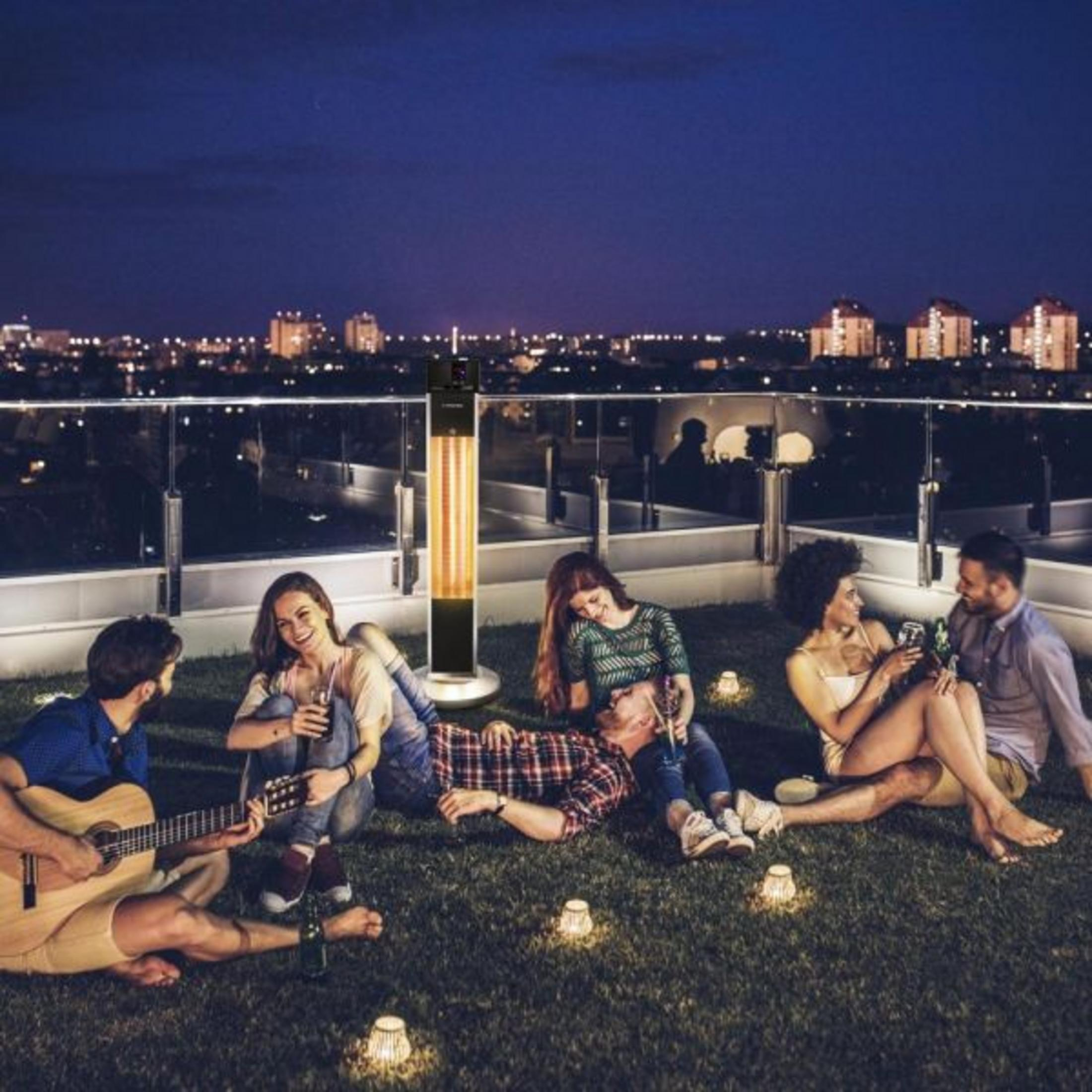 Gruppo di amici su una terrazza sul tetto di notte, con vista sulla città e riscaldatore.