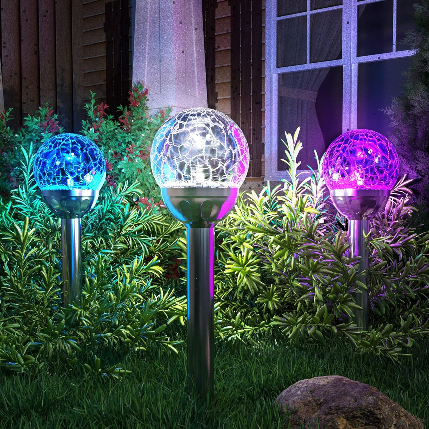 Drei leuchtende Glaskugellampen im Garten, blau, weiß und pink beleuchtet.