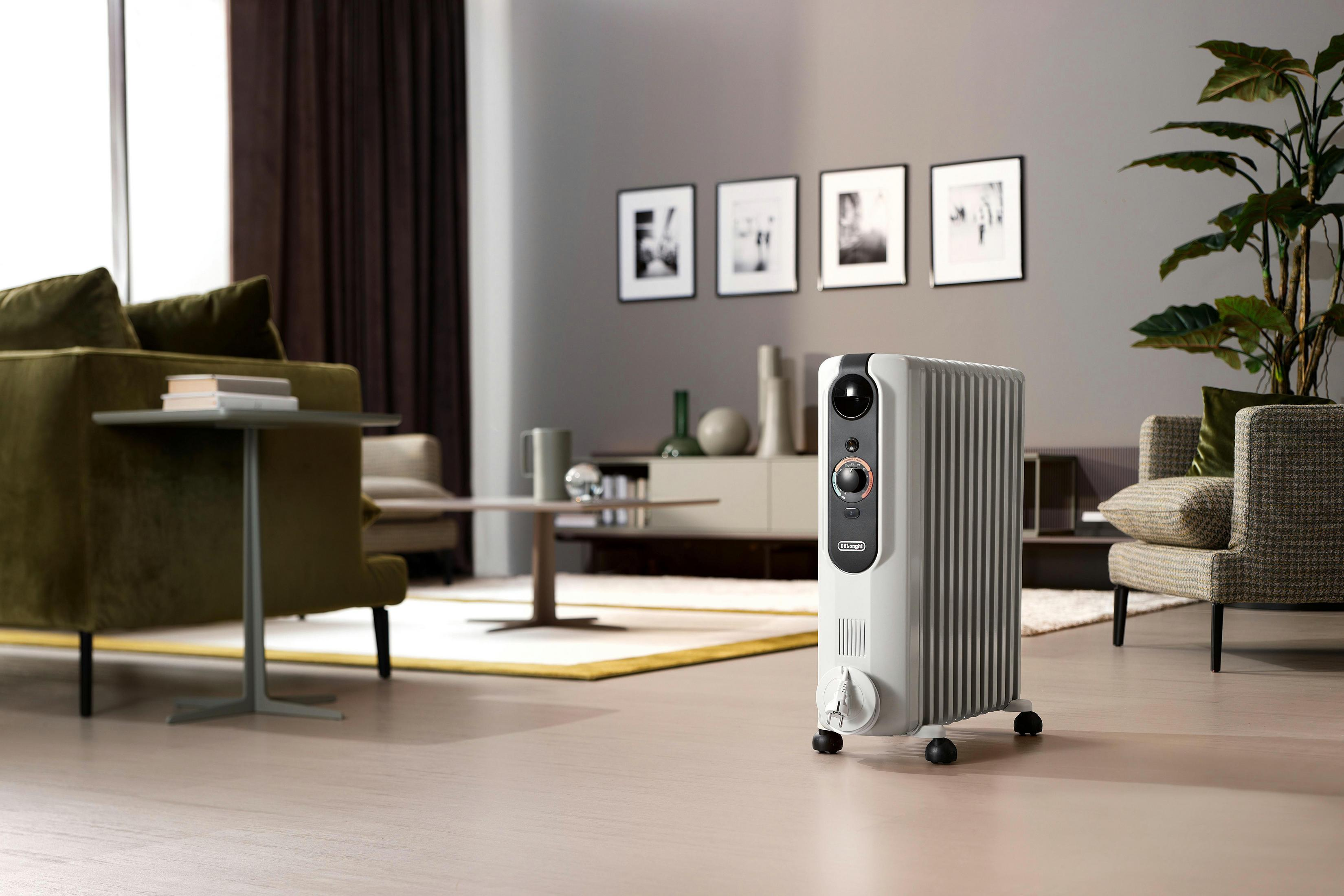 Biały grzejnik olejowy na kółkach stoi w salonie obok fotela.
