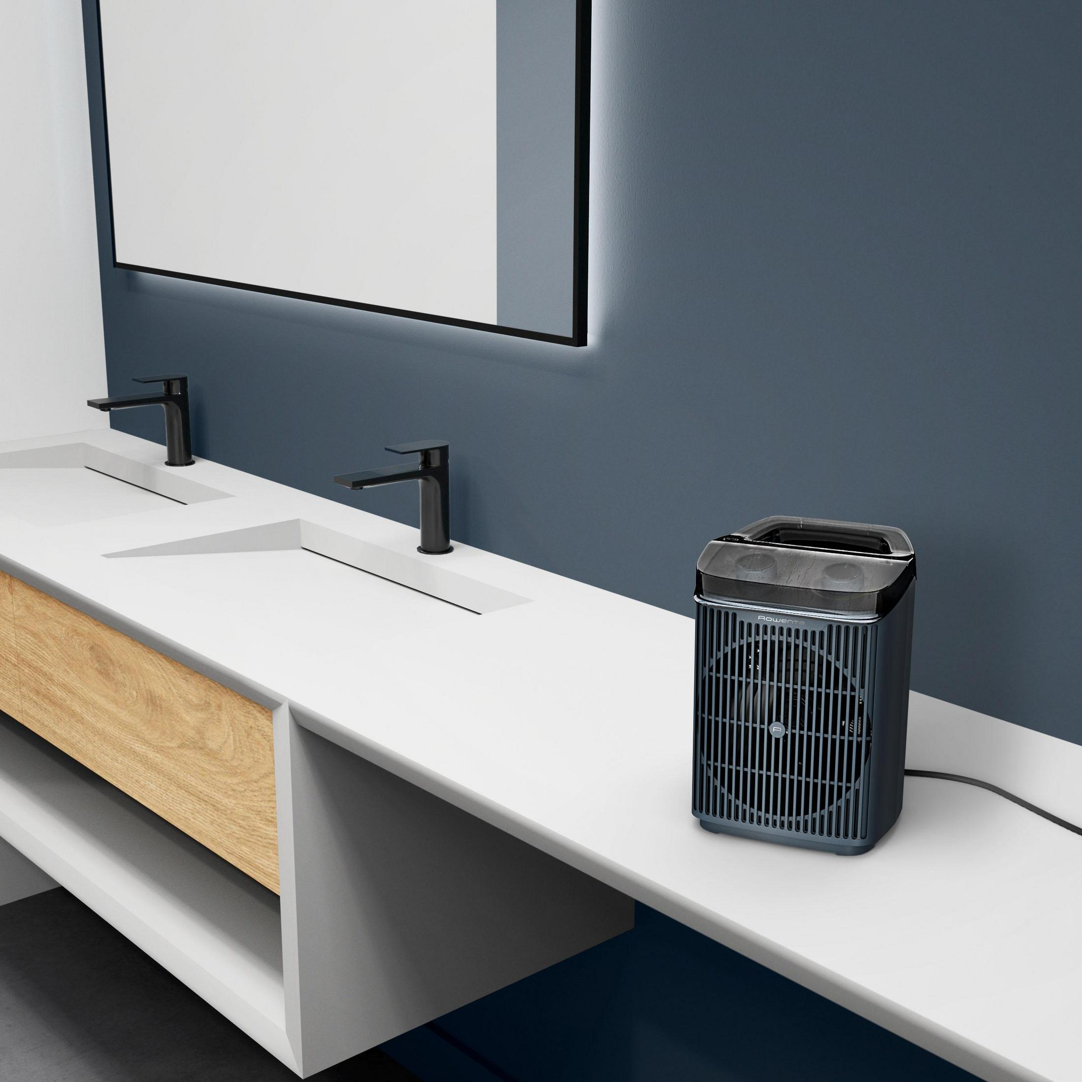 Czarny przenośny grzejnik stoi na białej toaletce obok dwóch umywalek.