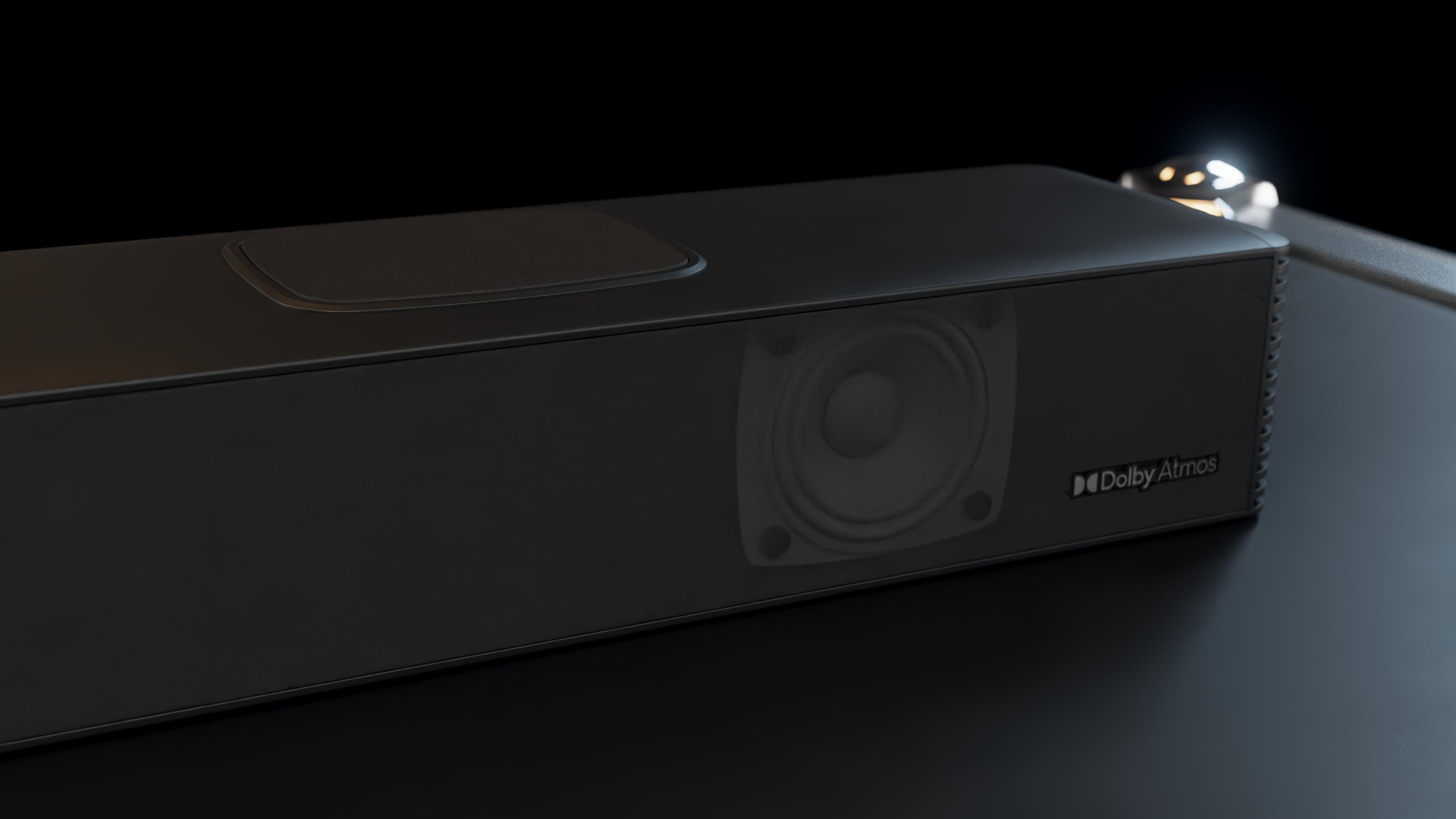 Barra de sonido negra con altavoz visible y logo Dolby Atmos sobre superficie oscura.