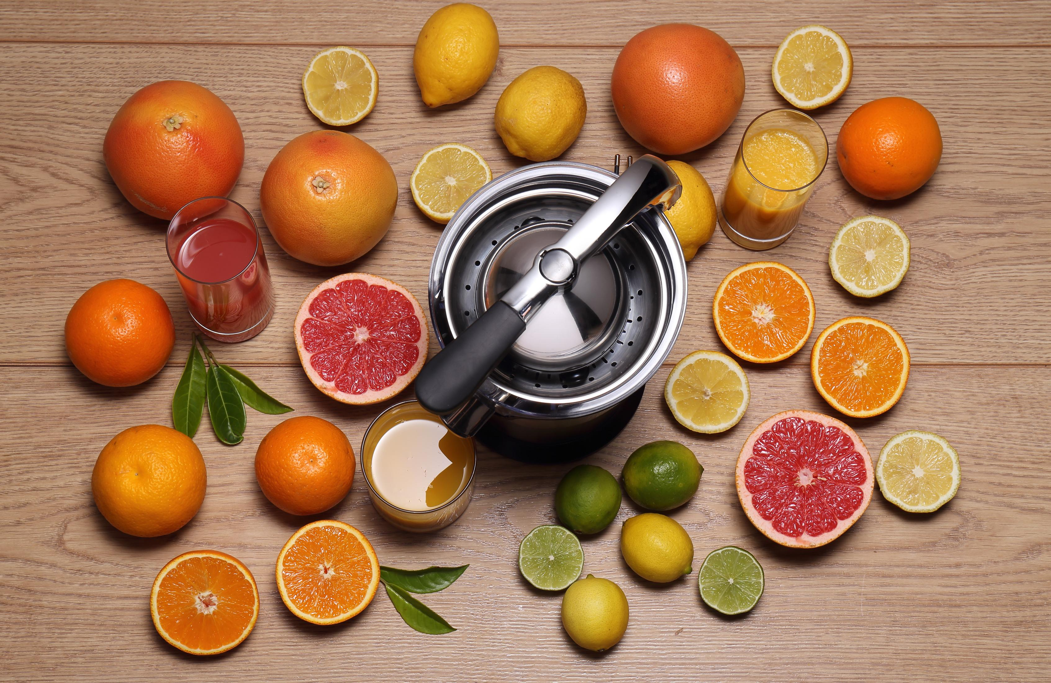 Früchte und Saftpresse auf Holztisch: Orangen, Zitronen, Grapefruits, Limetten.