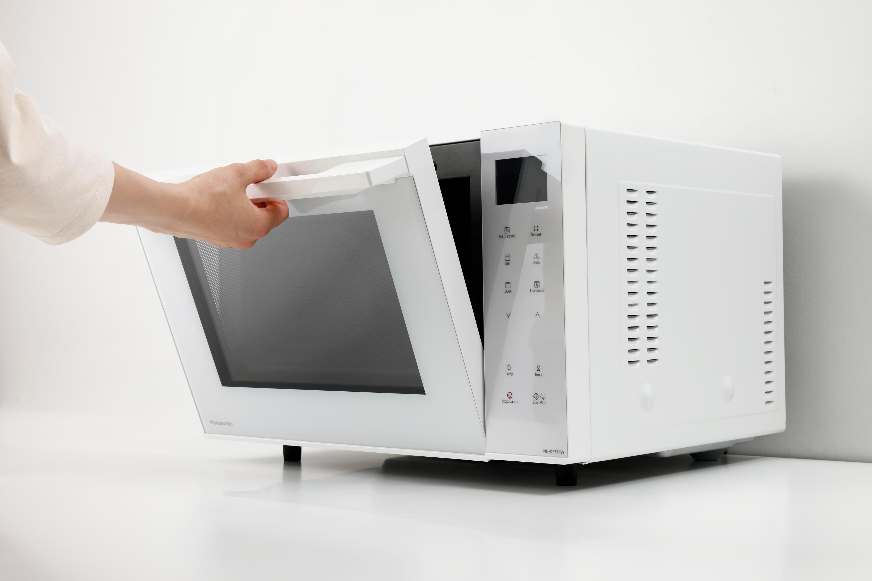 Biała kuchenka mikrofalowa z otwartymi drzwiczkami. Ręka otwiera drzwiczki.