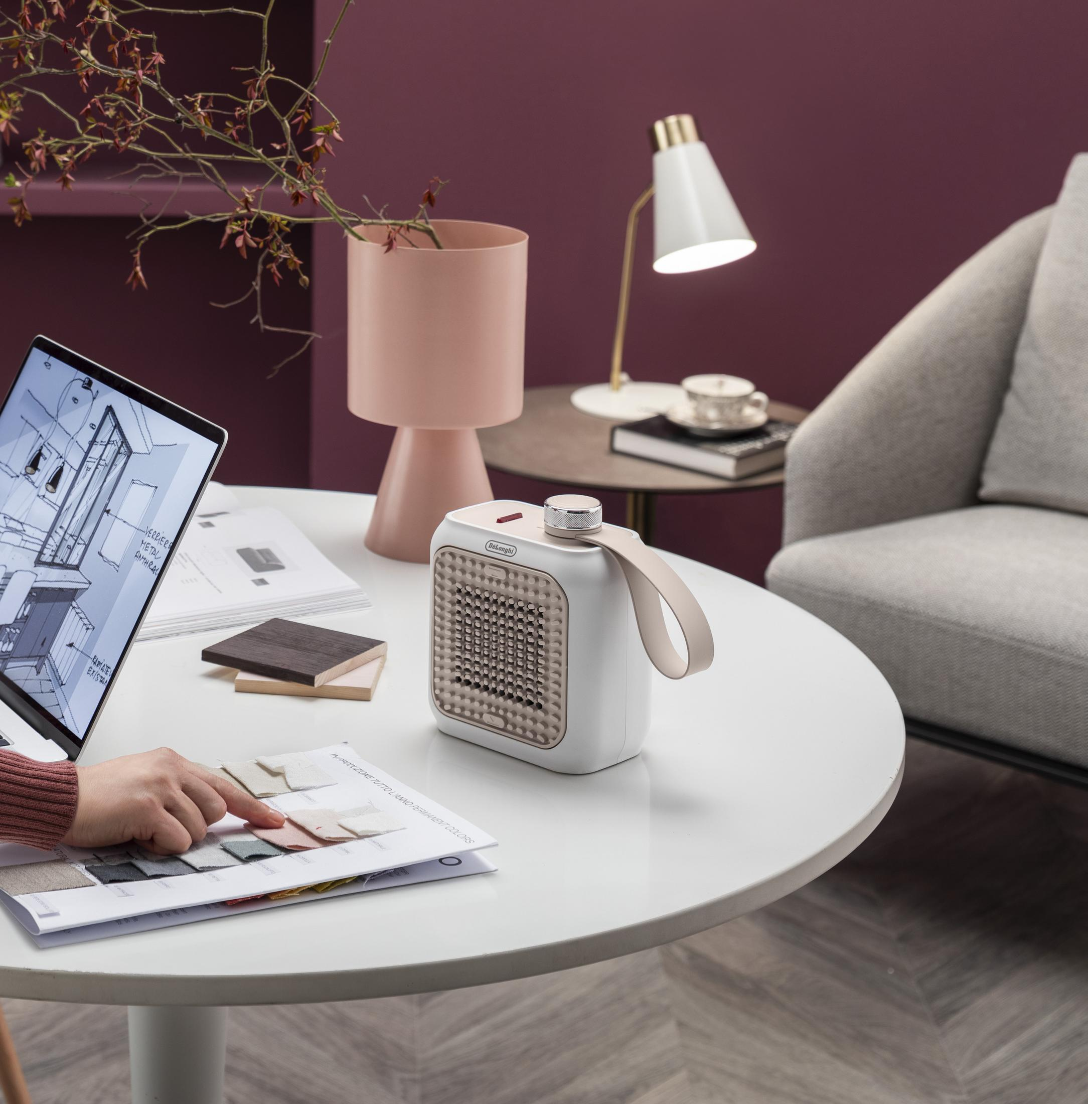 Osoba wybiera próbki tkanin obok grzejnika, laptopa i lampy.