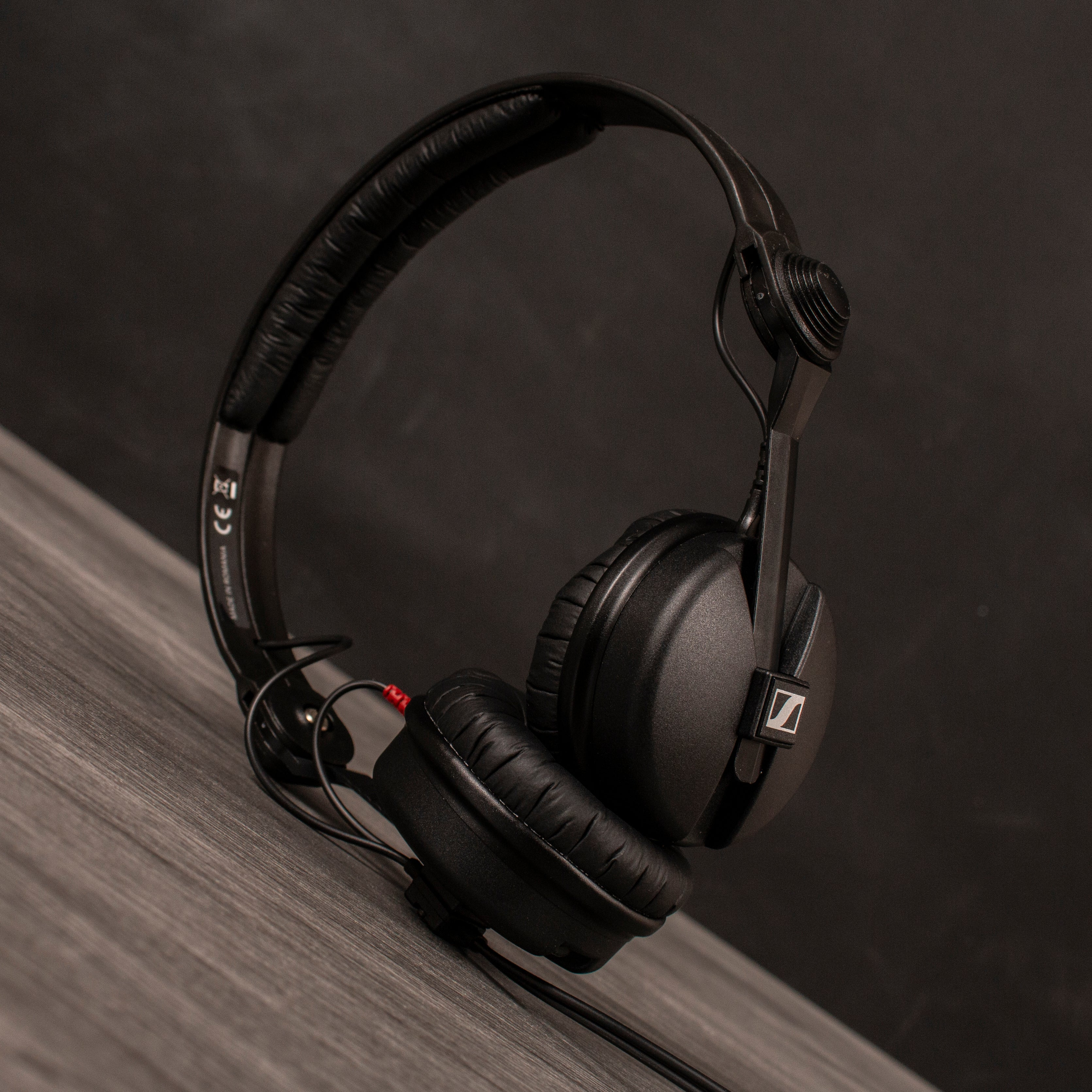 Black Sennheiser headphones with cable on a wooden table and dark background.
