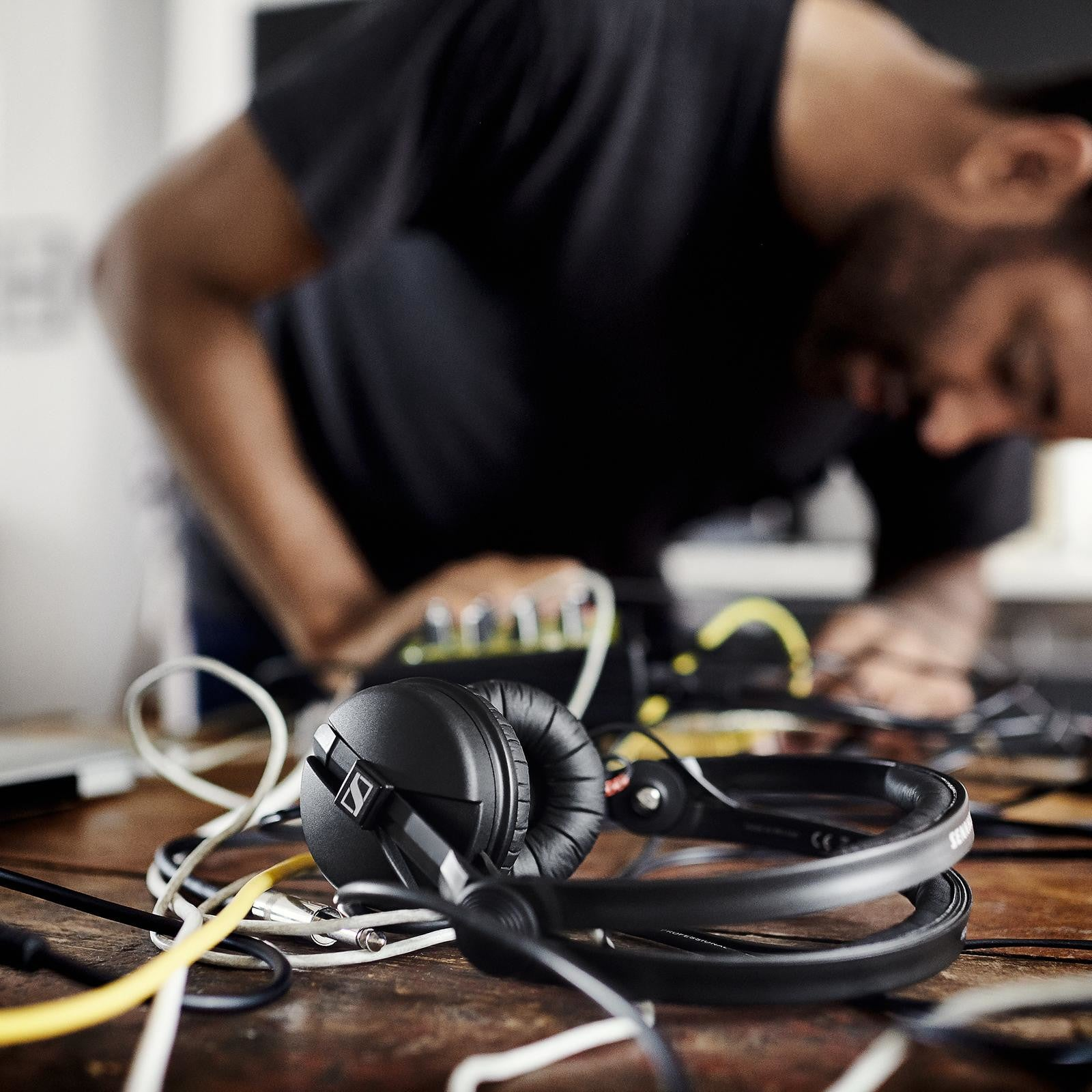 Black headphones rest on a wooden table amidst tangled cables.