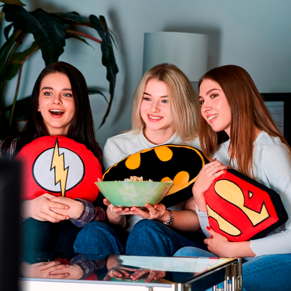 Tre giovani donne guardano la TV, tengono cuscini da supereroe e una ciotola di popcorn.