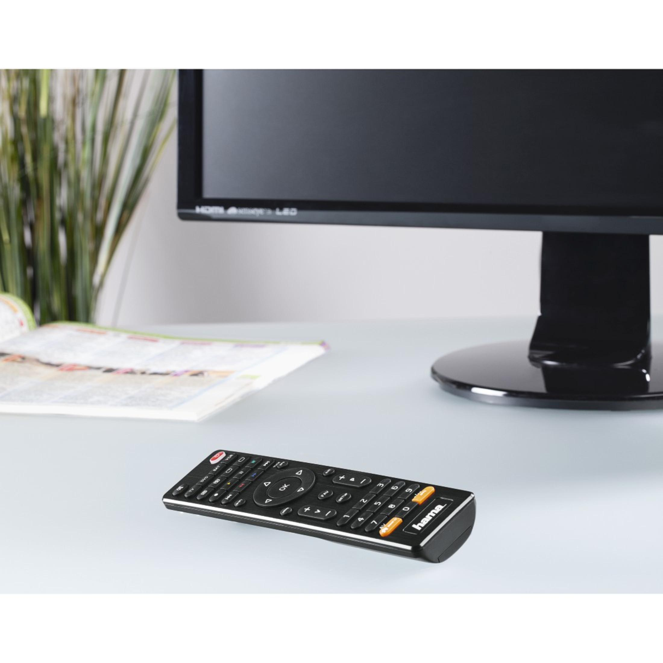 Czarny pilot z pomarańczowymi przyciskami leży na stole obok monitora.