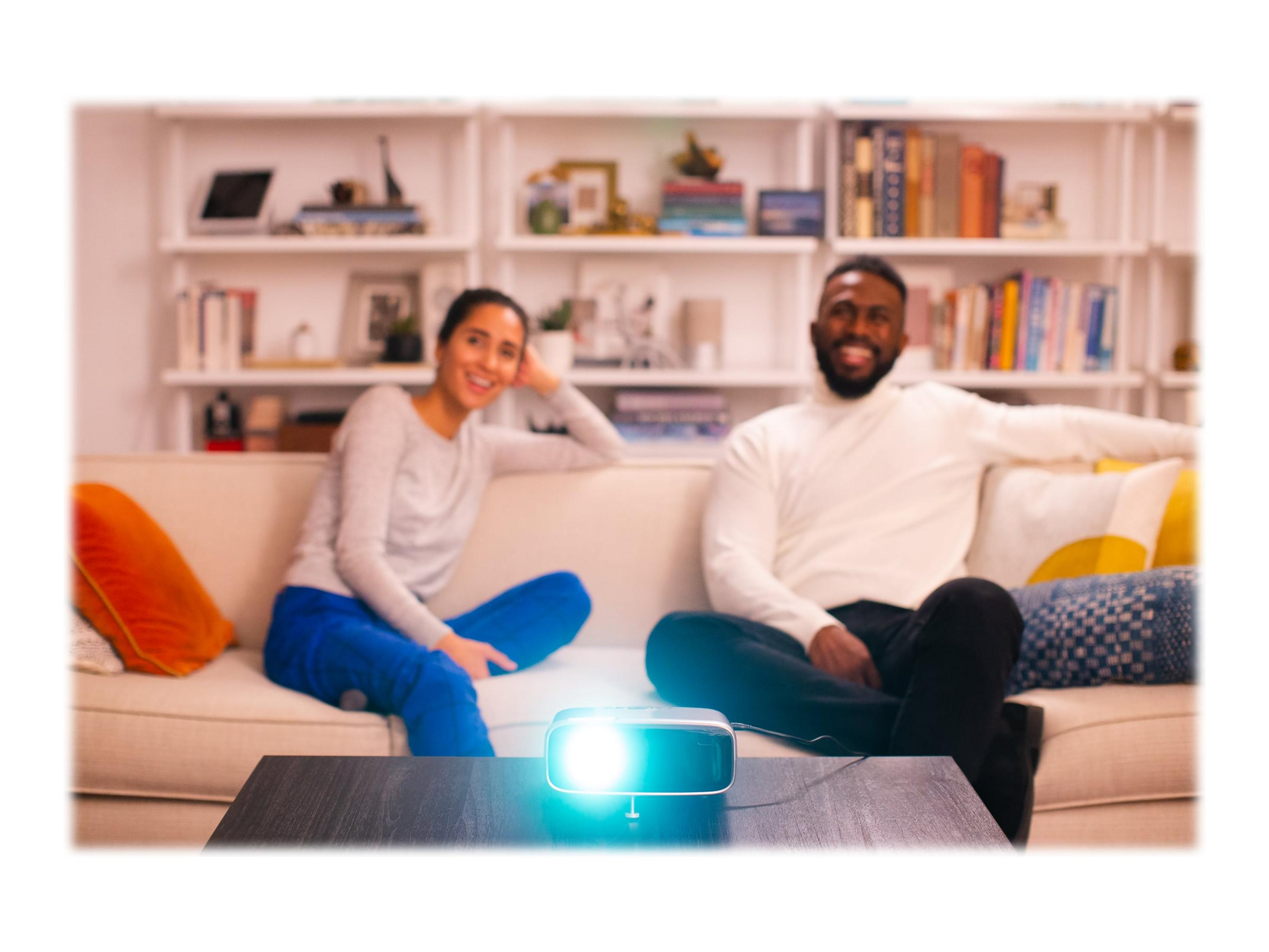 Una pareja se relaja en un sofá, un proyector brilla intensamente.