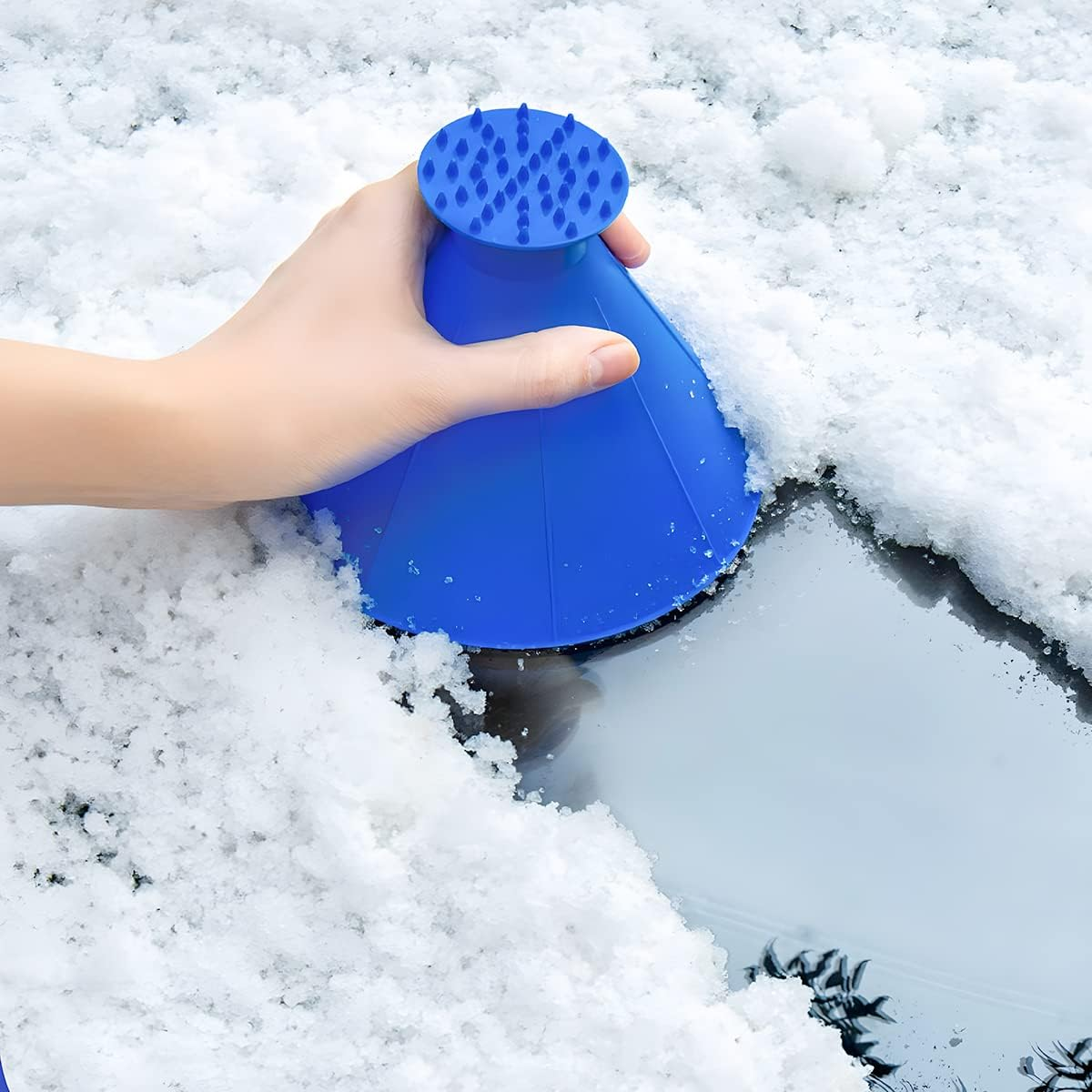 Eine Hand hält einen blauen Eis-/Schneekratzer, um Schnee von einer Glasoberfläche zu entfernen.