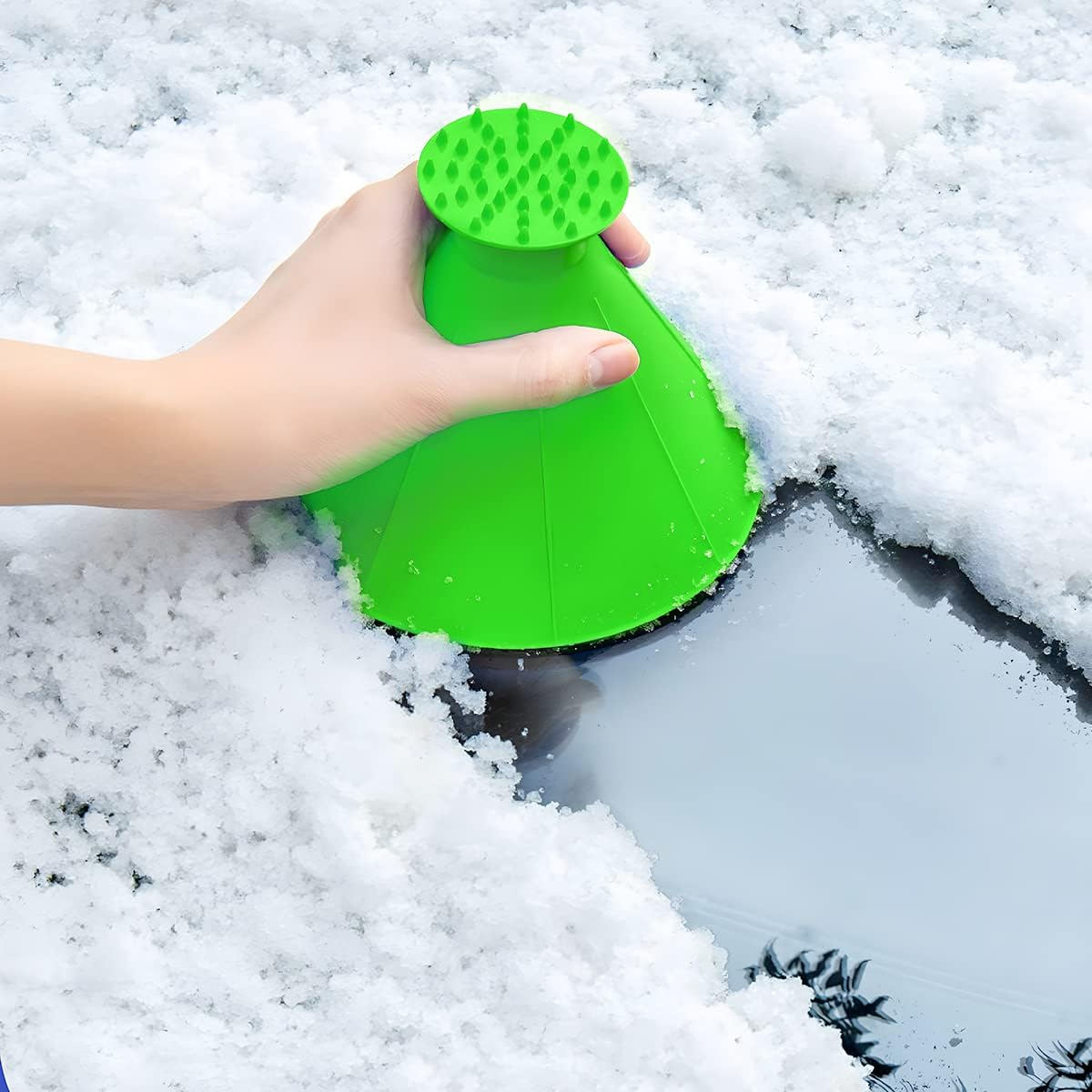 Grüner Eis-/Schneeschaber, der von einer Hand gehalten wird, um Schnee von einer Scheibe zu entfernen.