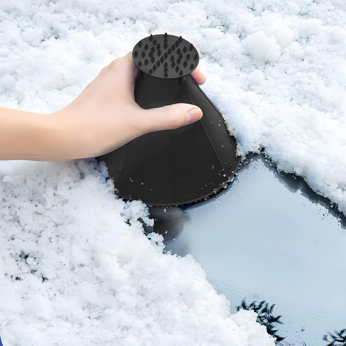 Eine Hand hält einen schwarzen Eis-/Schneeschaber, um Schnee von einer Glasoberfläche zu entfernen.