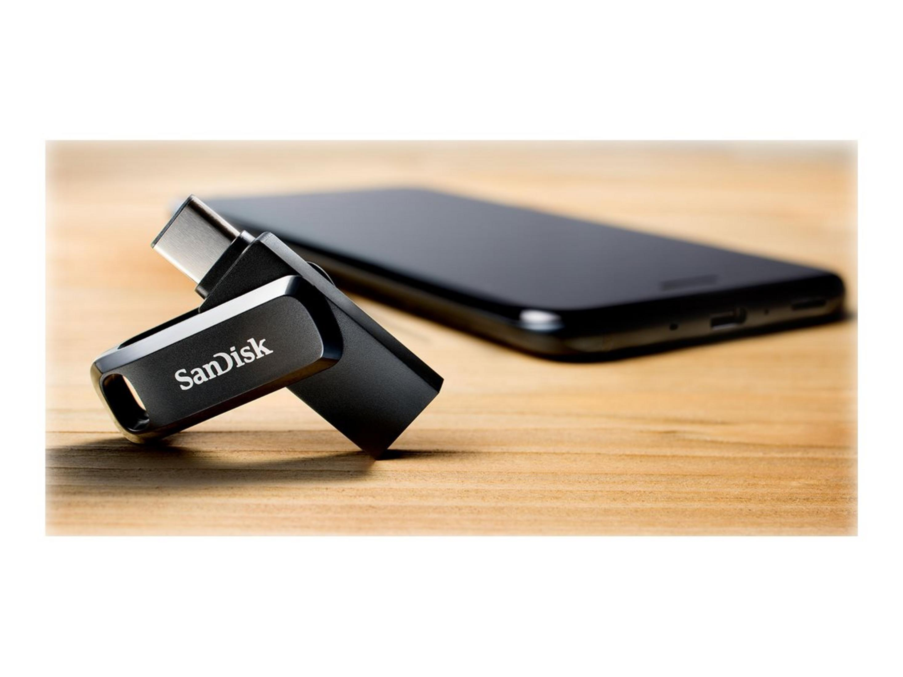 A black SanDisk USB-C flash drive rests beside a smartphone.