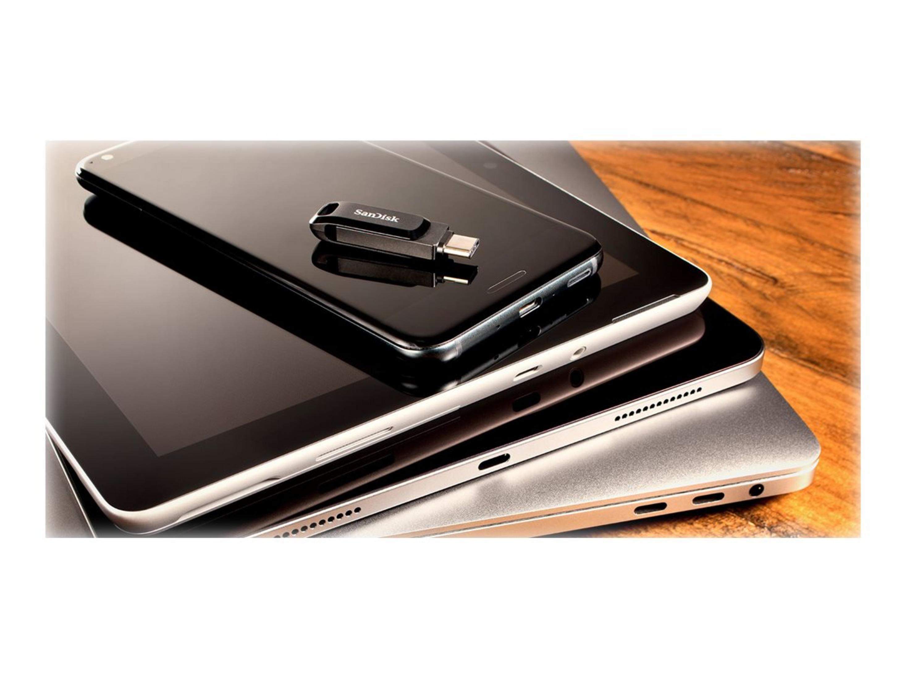 A USB drive rests on a smartphone stacked on a tablet and laptop.