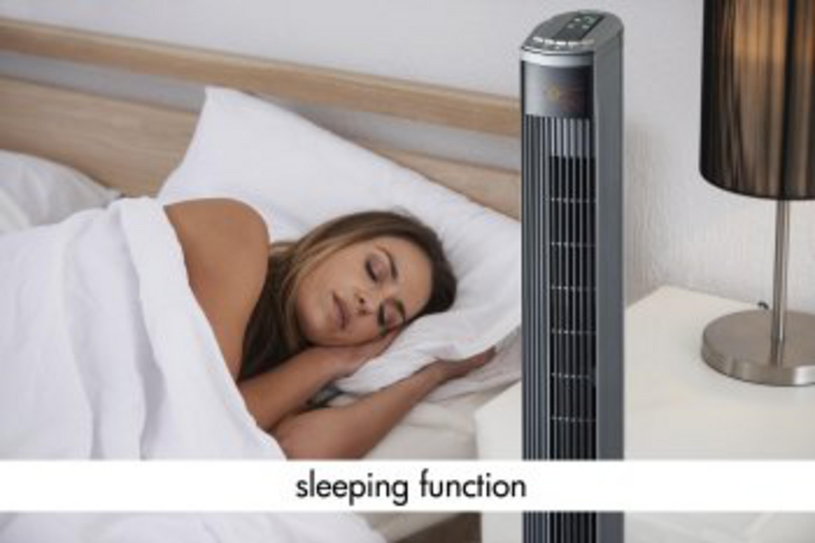 Frau schläft im Bett neben einem Turmventilator und einer Lampe.