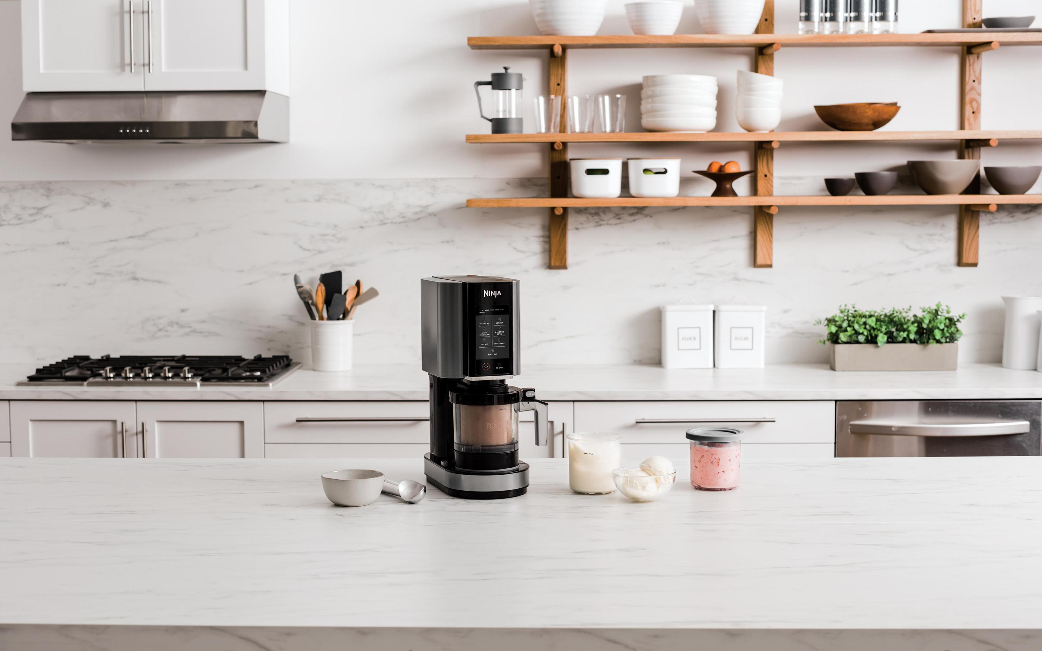 A kitchen machine with ice cream, a bowl, and a spoon on a marble countertop.